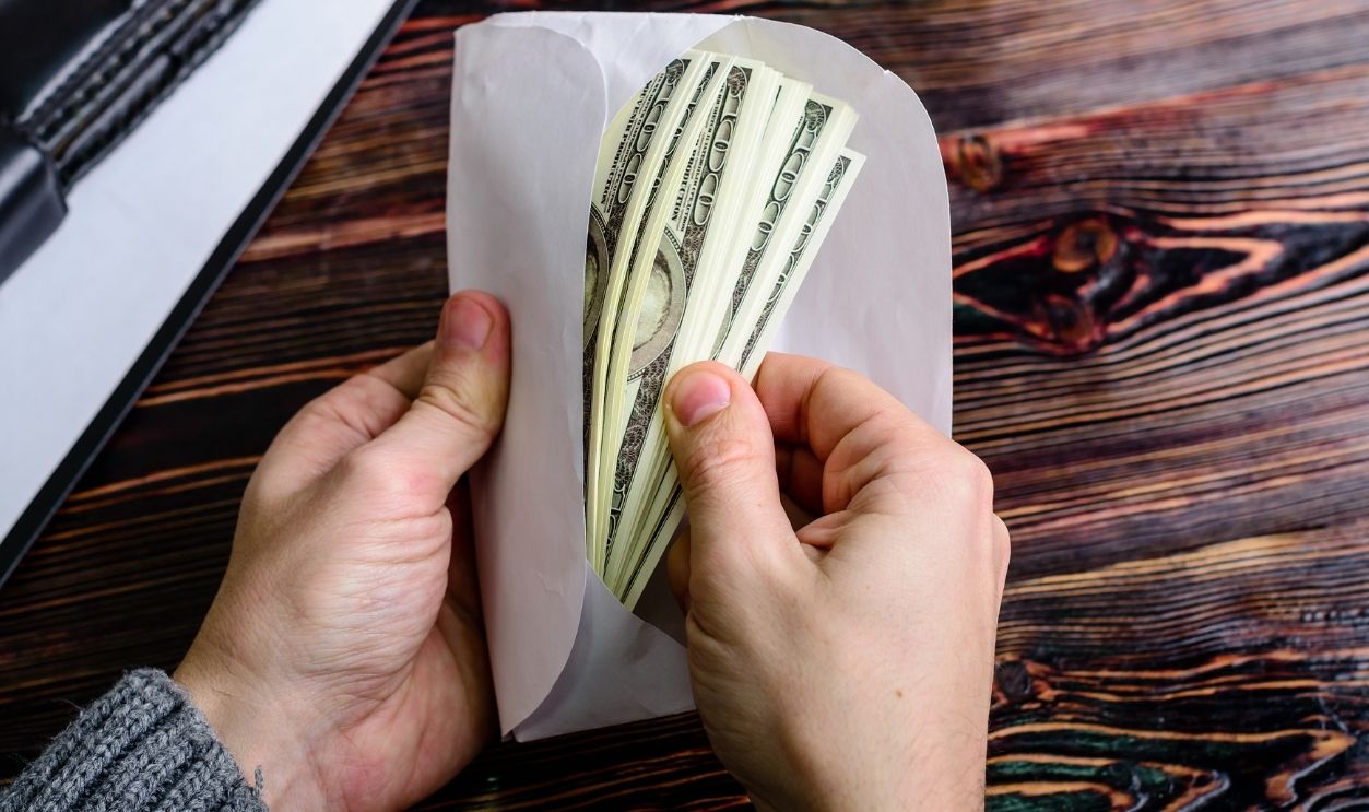 Man counting money, US dollars, in the envelope just given by his partner - bribery and corruption concepts