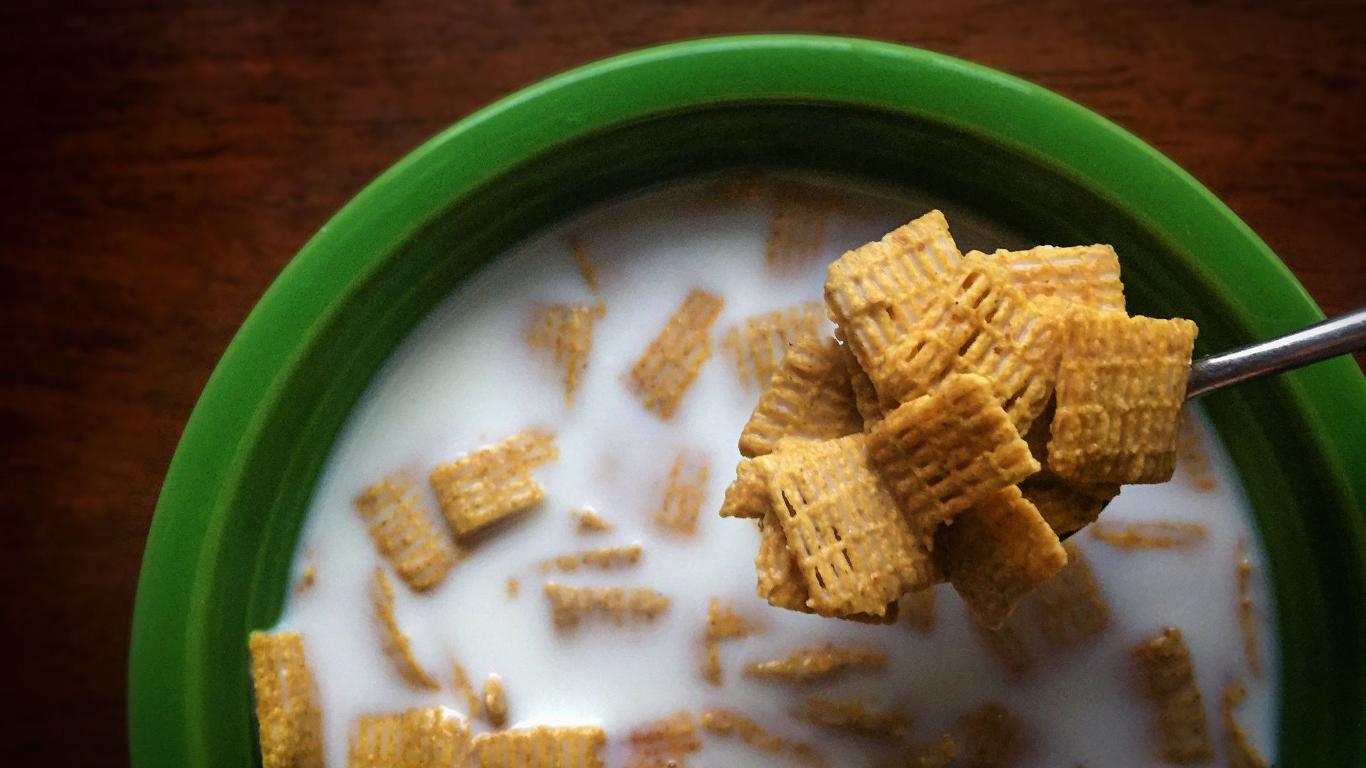 Top view of Chex cereal in milk inside a green bowl, showcasing a spoonful of cereal.