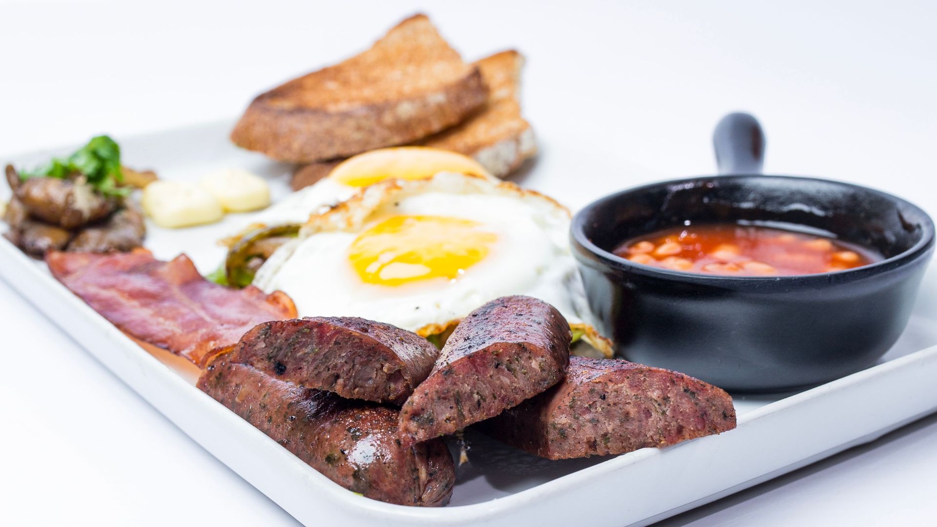 Delicious English breakfast featuring eggs, sausages, bacon, and toast served with a side of sauce.