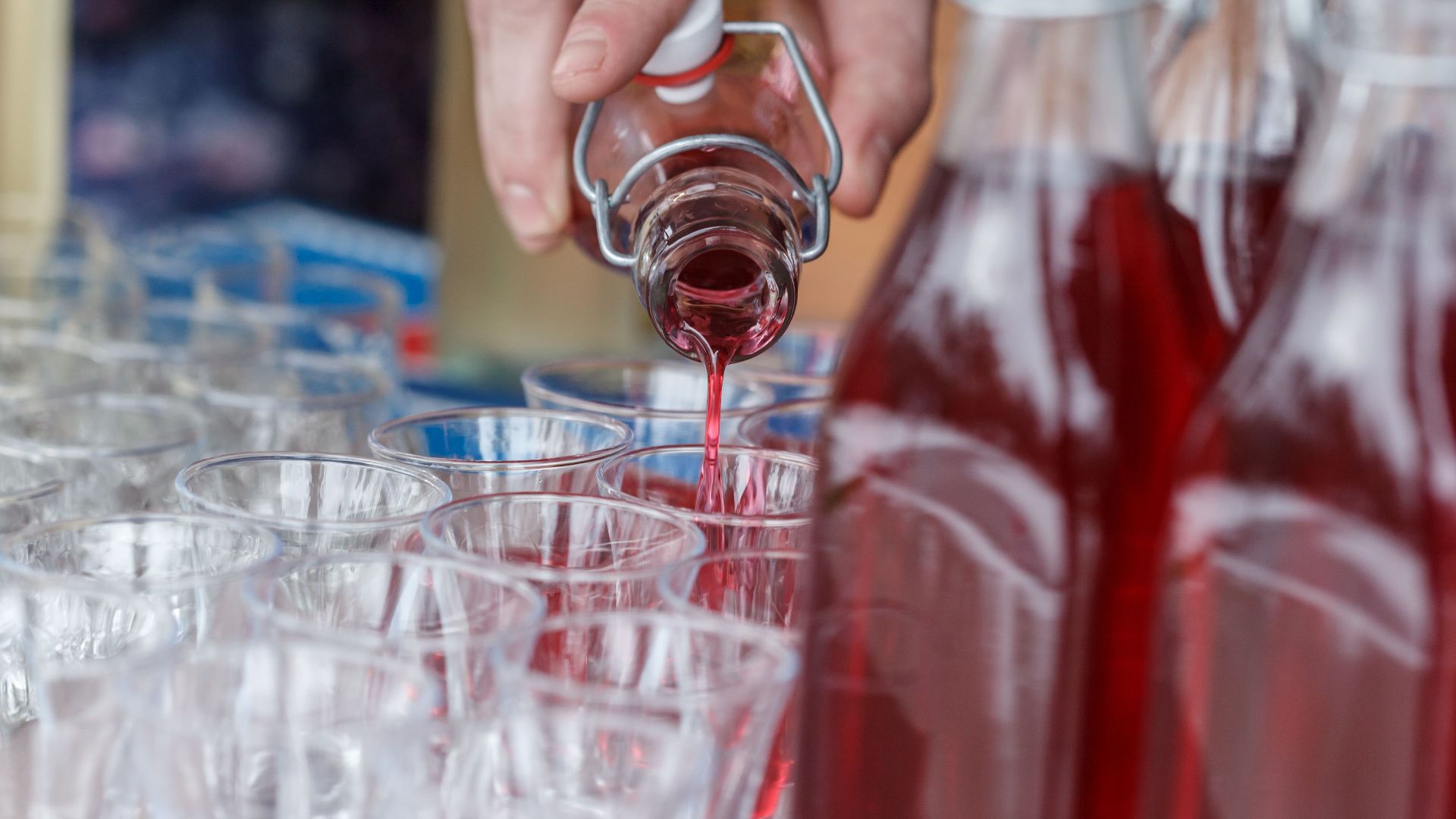 Hand pouring vibrant red liquid into multiple shot glasses, perfect for party or celebration themes.