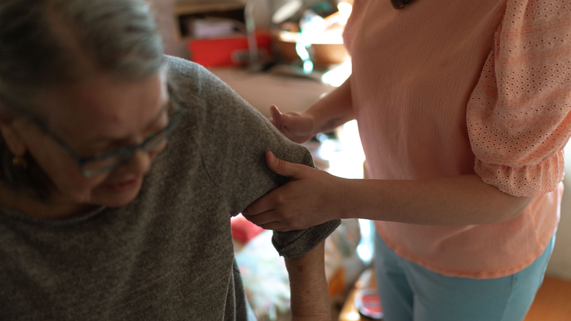 Compassionate caregiver helps elderly woman with mobility at home, offering caring support.