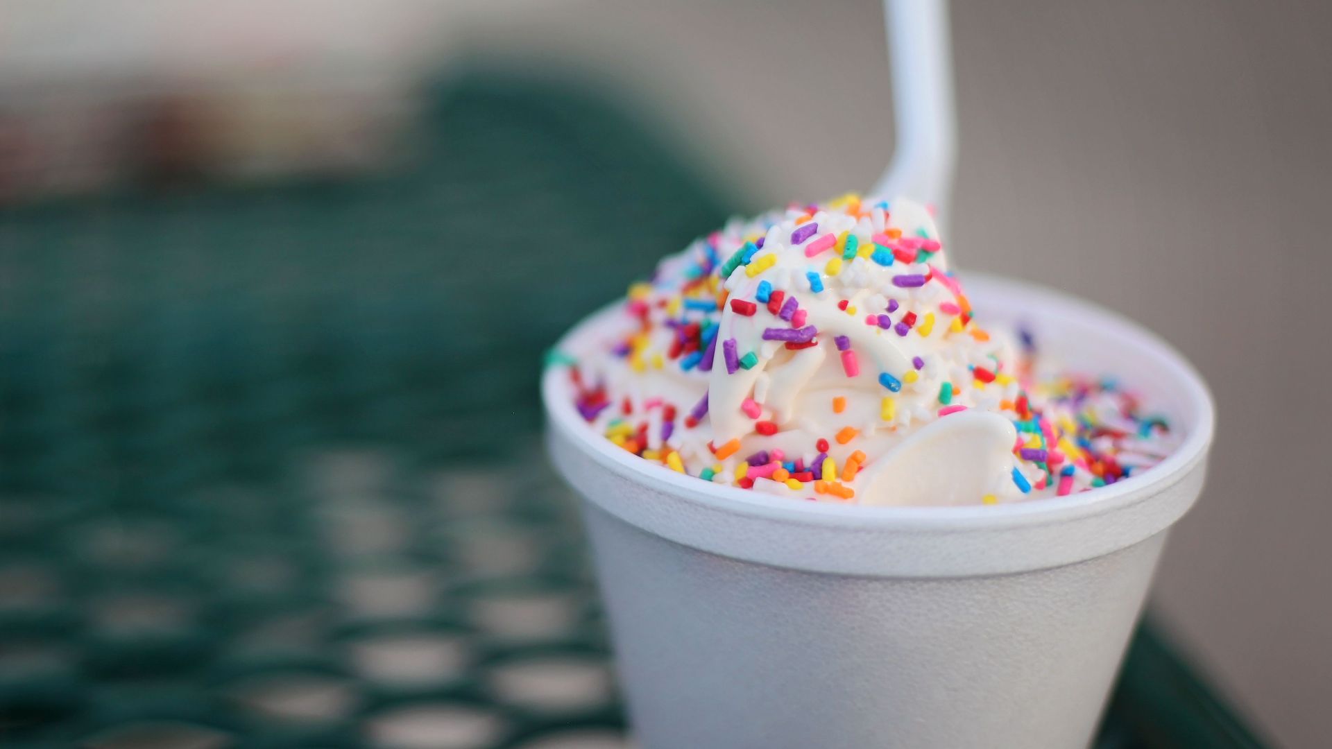 Indulgent vanilla ice cream with colorful sprinkles in a cup on an outdoor table.