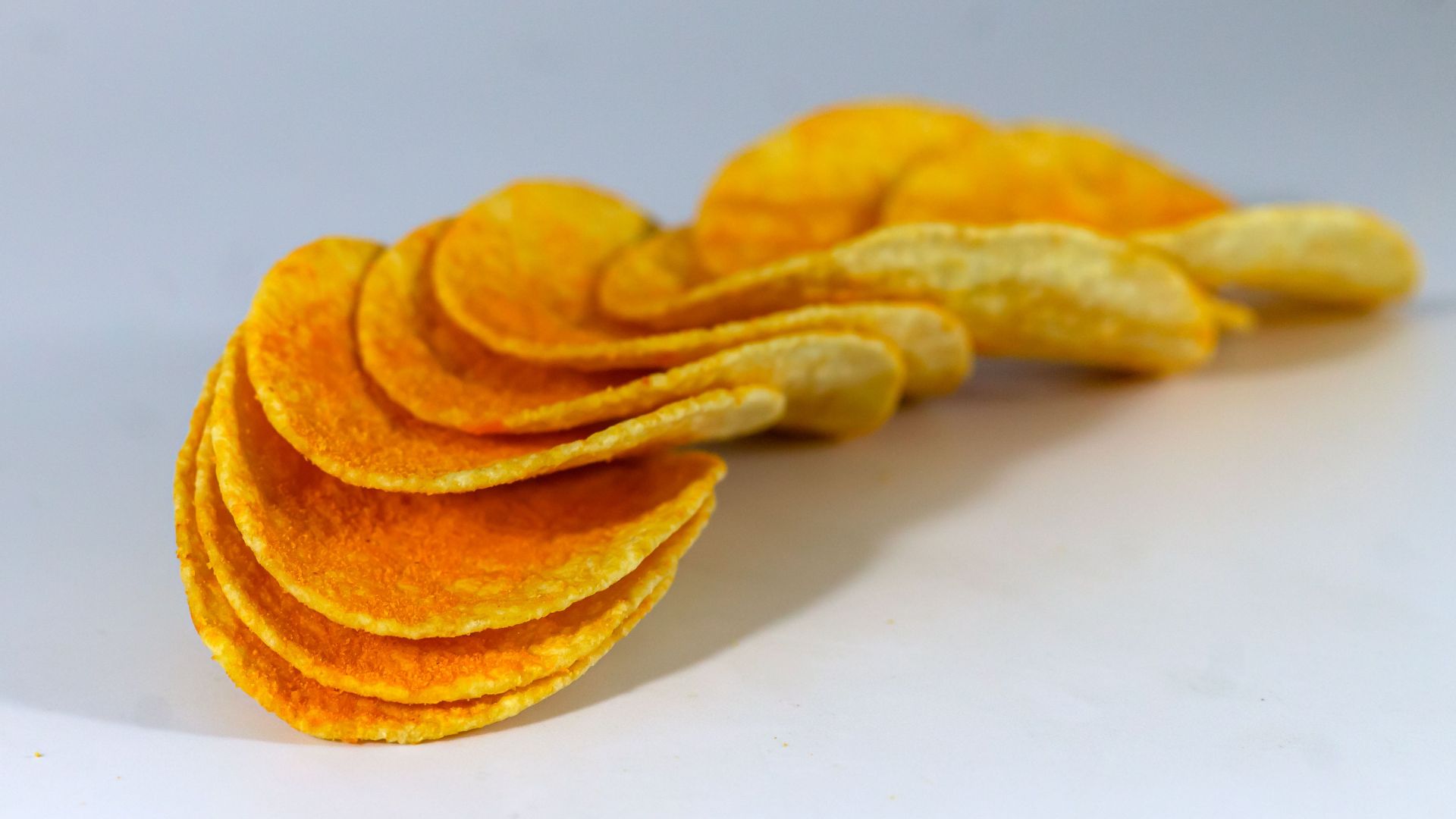 A detailed close-up of crunchy potato chips arranged in a curve on a white background.