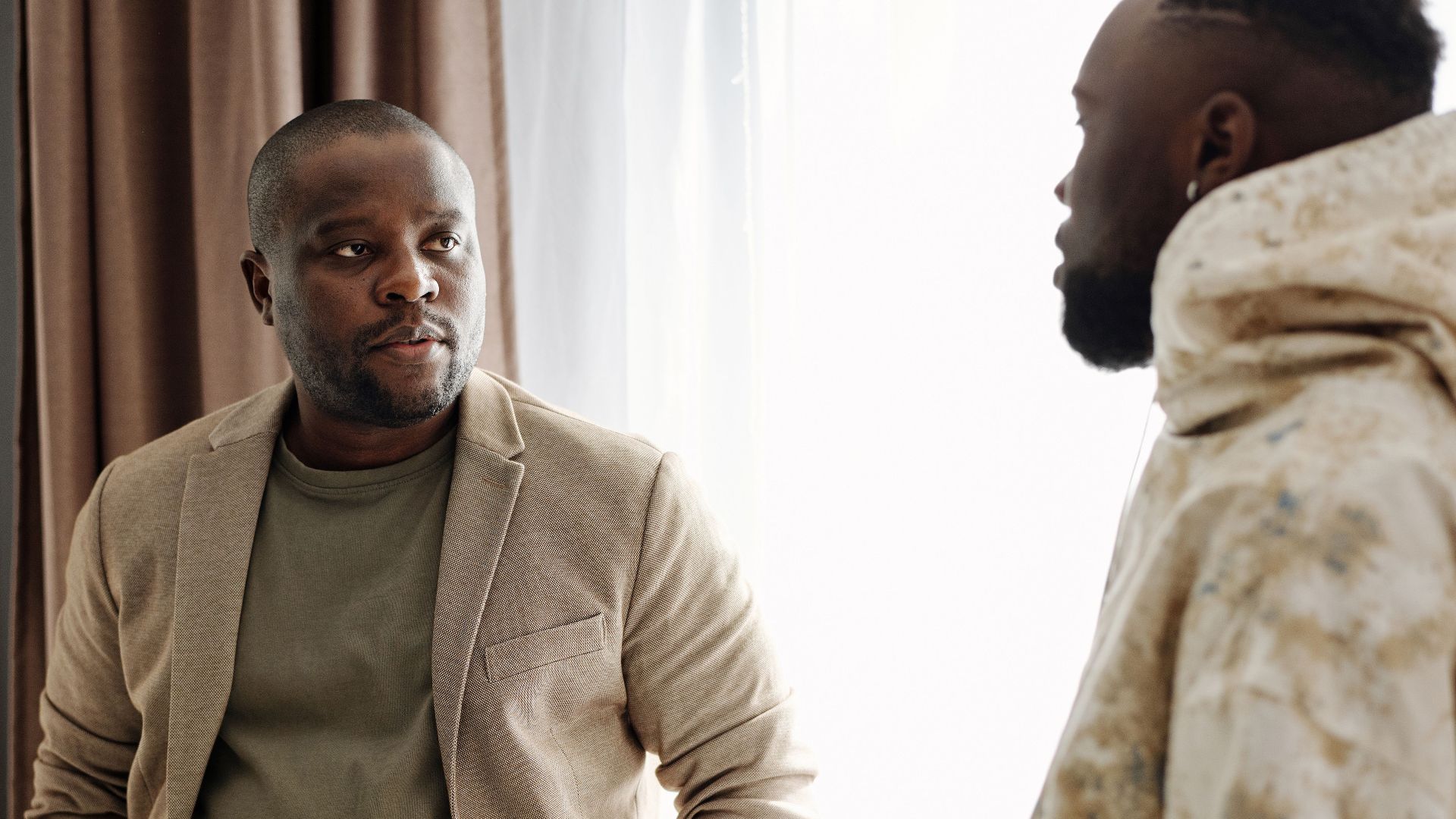 Two men engaged in a serious conversation indoors, one holding a smartphone.