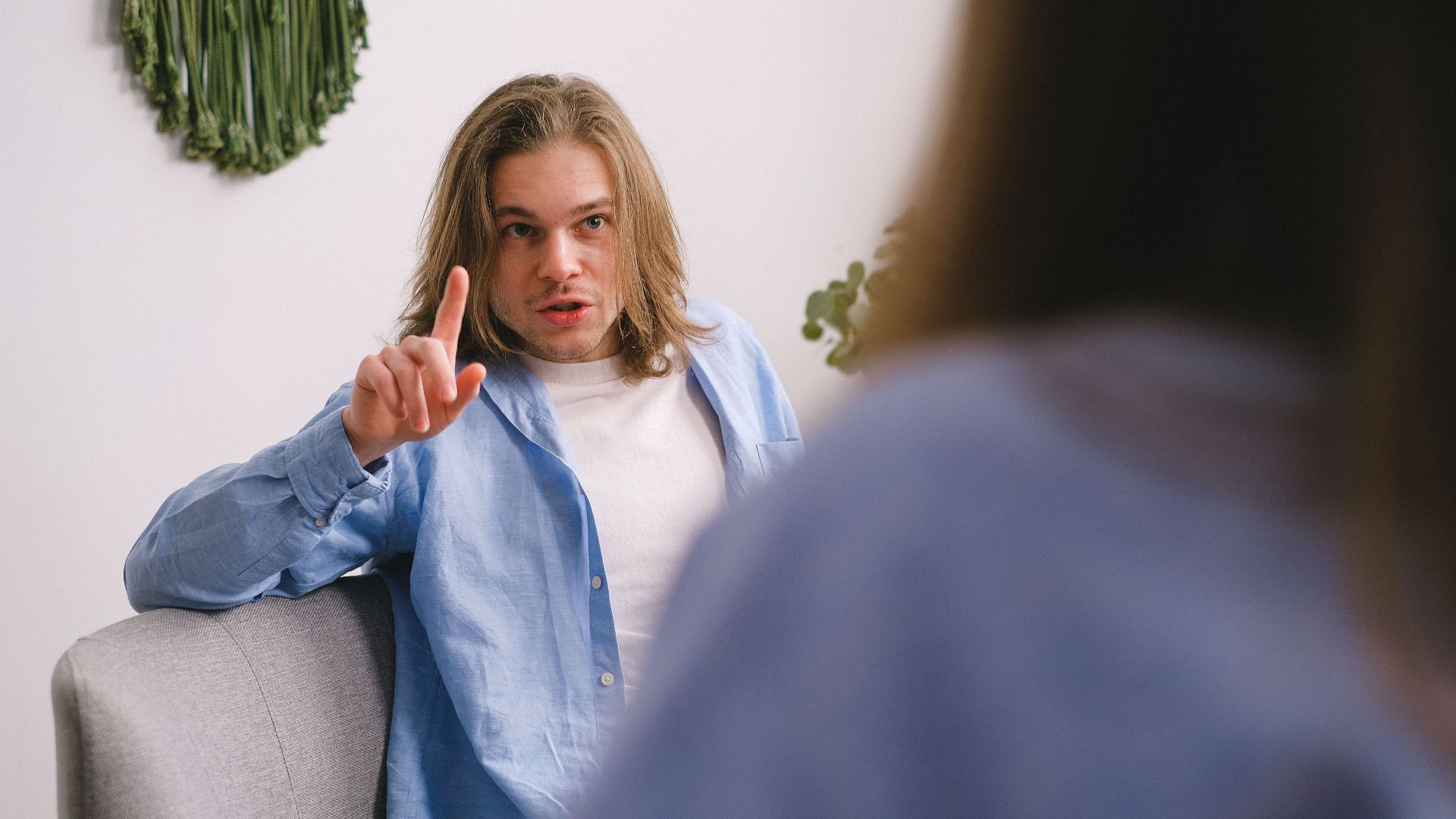 A therapist gestures while talking to a patient in a relaxed indoor environment.