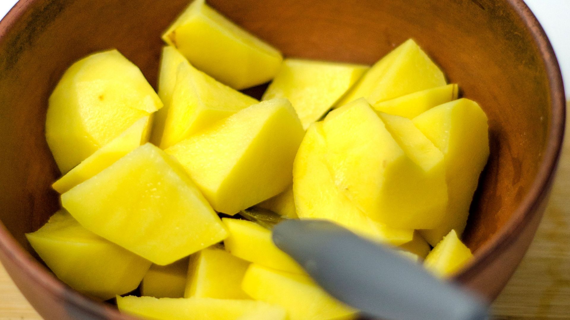 Freshly peeled and chopped potatoes in a wooden bowl on a cutting board, perfect for food photography.