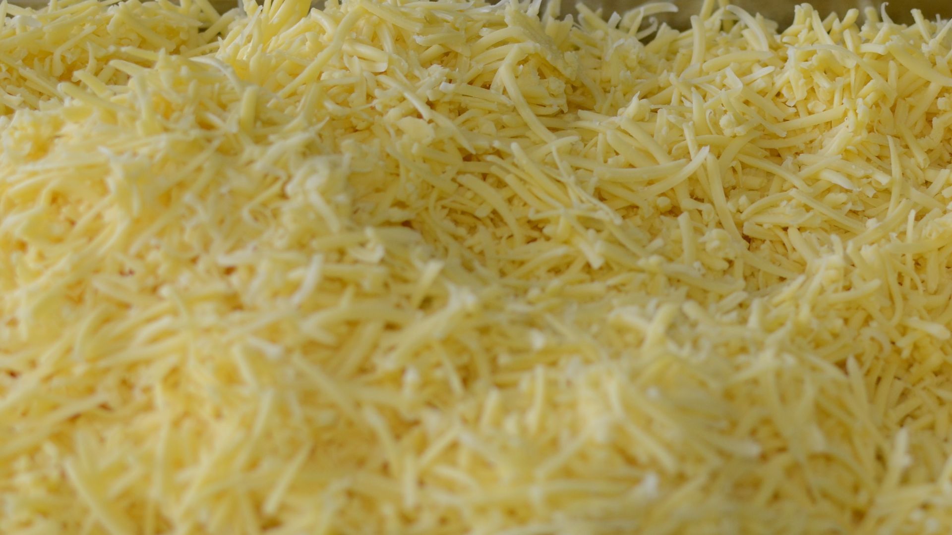 Close-up of shredded cheese and sliced onions in metal trays, perfect for cooking or catering setups.