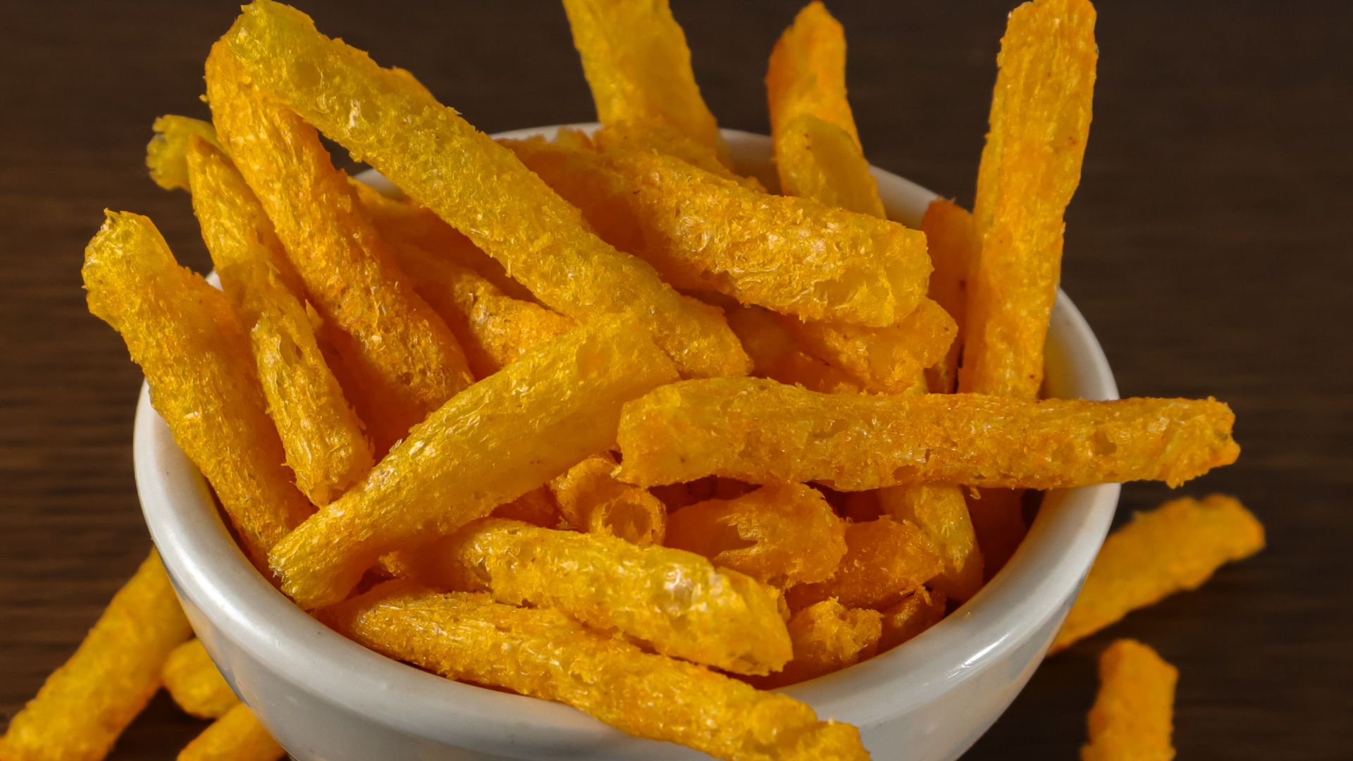 Close-up of crispy cheese sticks in a white bowl on a wooden table, perfect for snack time.