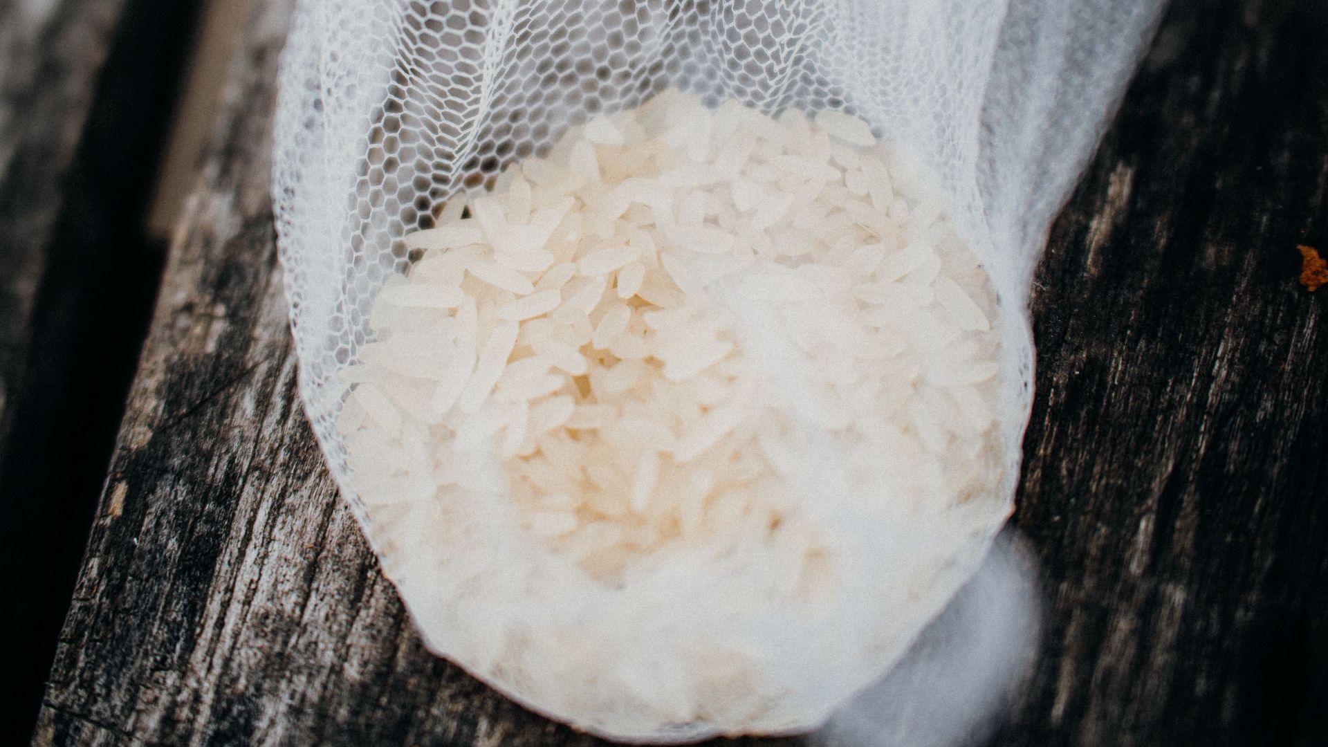 A close-up of rice grains wrapped in a mesh net on a rustic wooden surface.