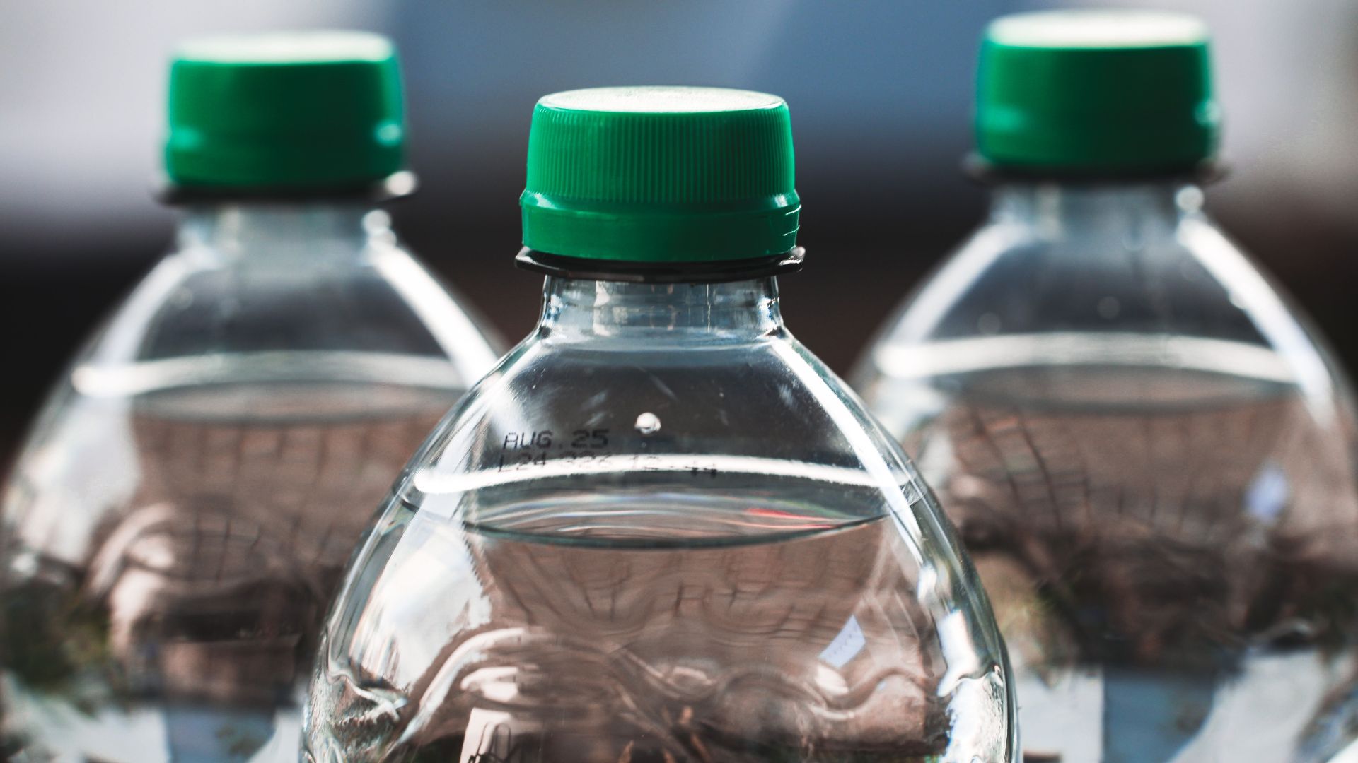 Focused view of three clear plastic bottles with green caps outdoors.
