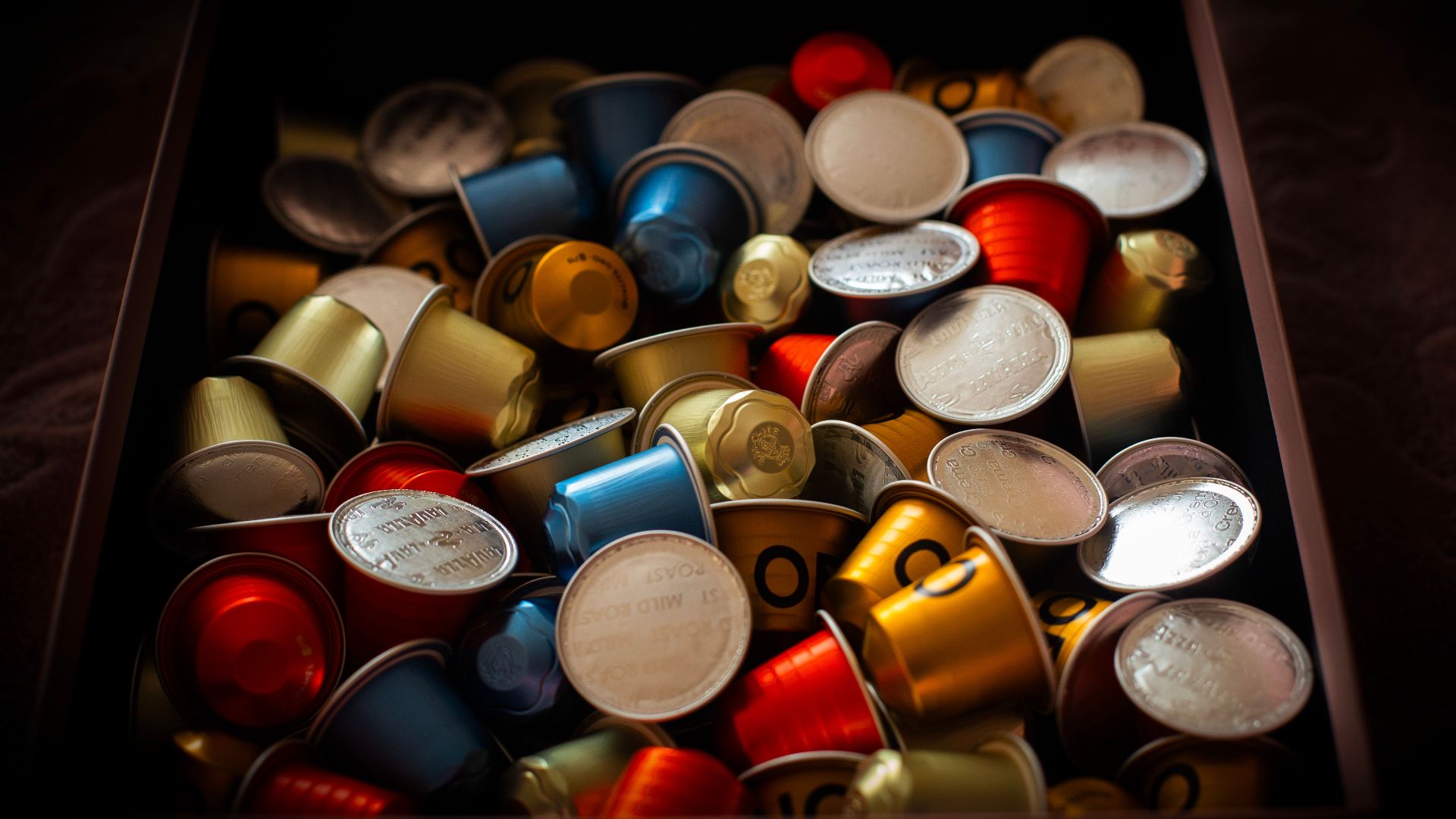 Vibrant collection of coffee capsules overflowing in a dark box, creating a colorful and rich visual.