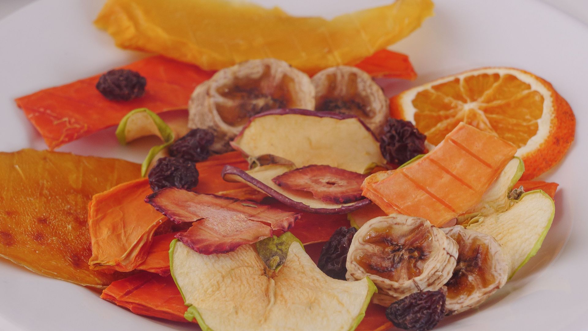 Colorful array of dried fruits including oranges and apples on a white plate.