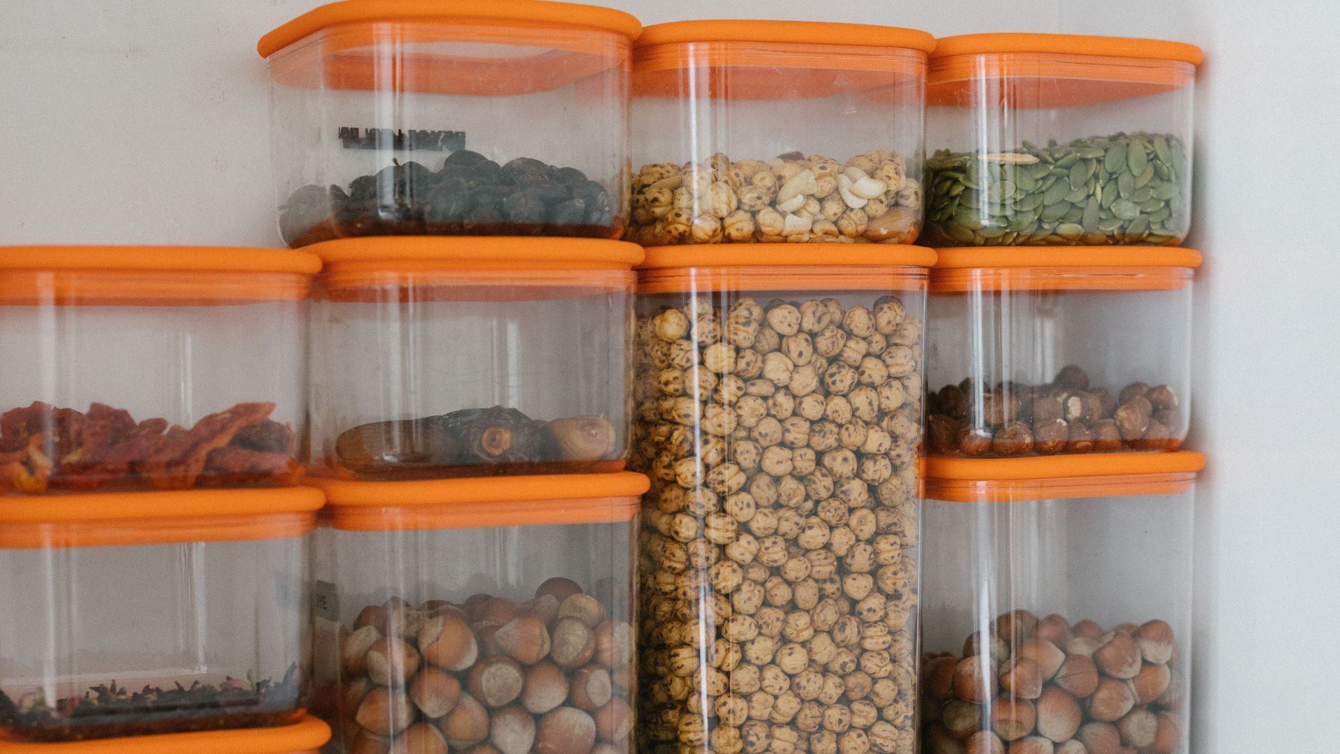 Various nuts and grains stored in transparent plastic containers with orange lids, organized neatly.