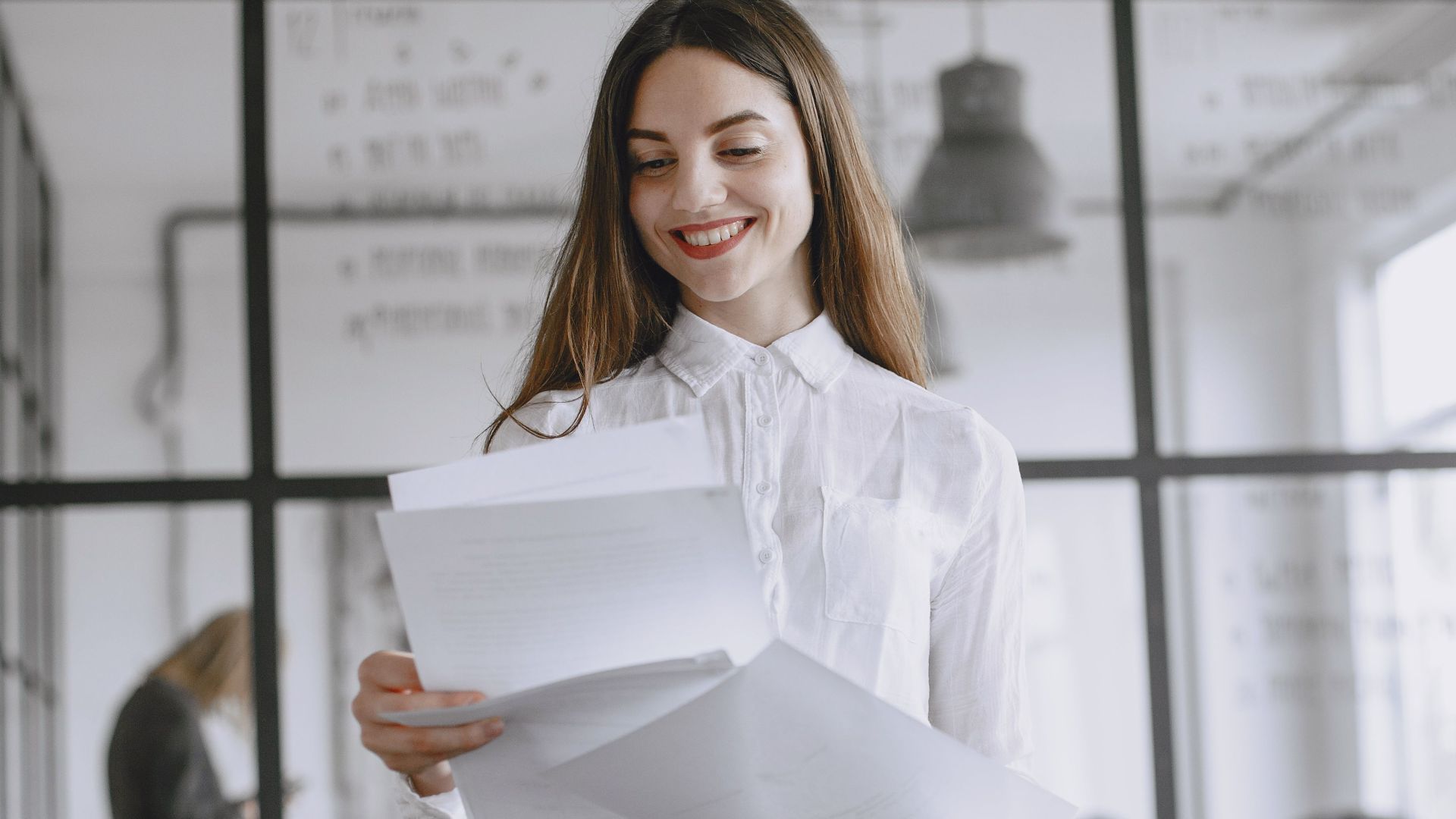 Confident woman with long hair reviewing documents at modern office desk.
