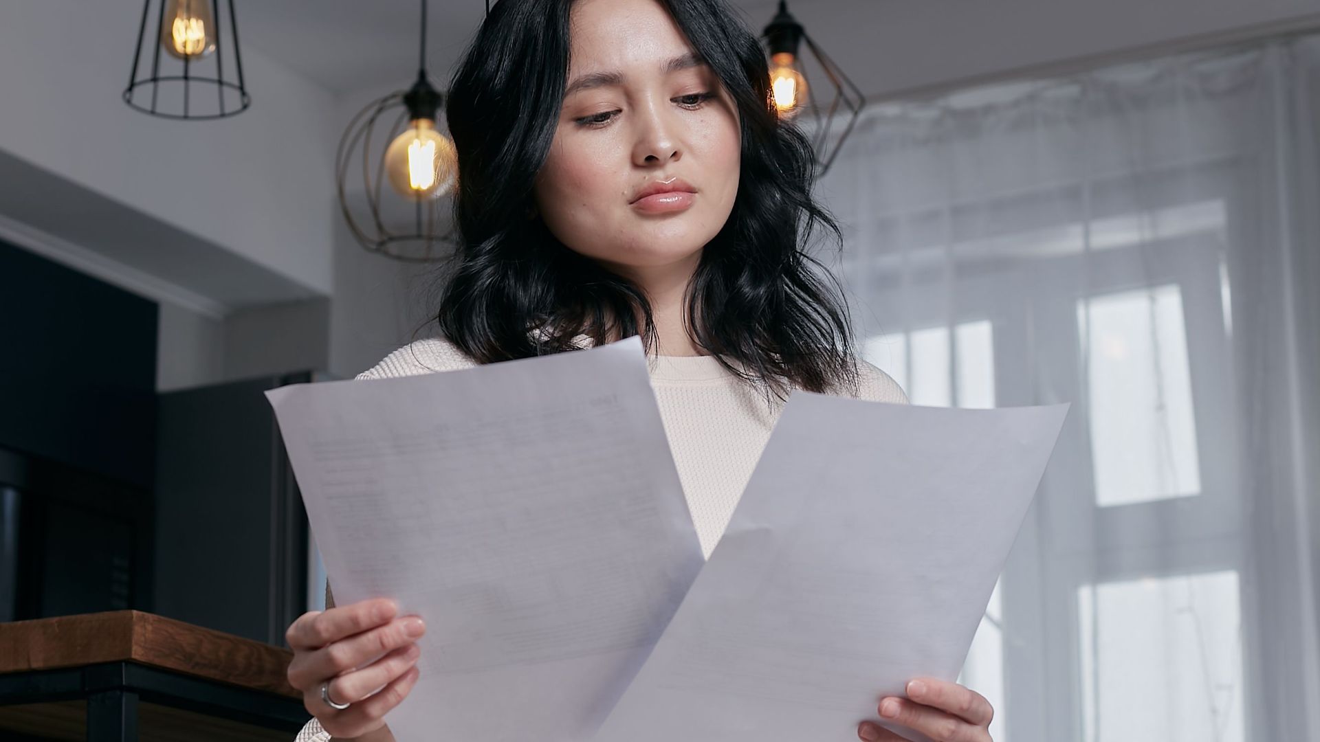 A woman sitting indoors, carefully reviewing papers under a stylish lighting setup.