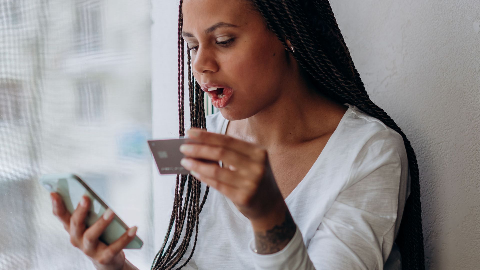 African woman using smartphone and credit card at home.