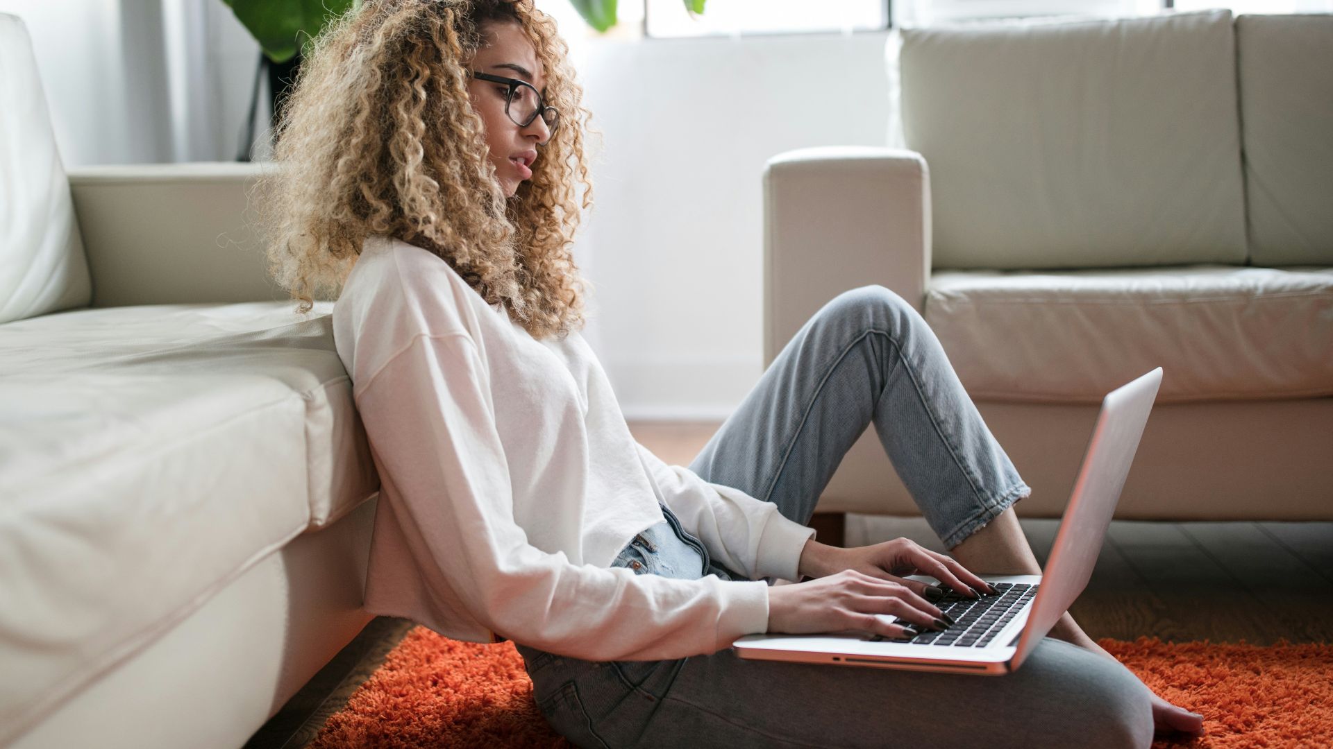 woman sitting on floor and leaning on couch using laptop