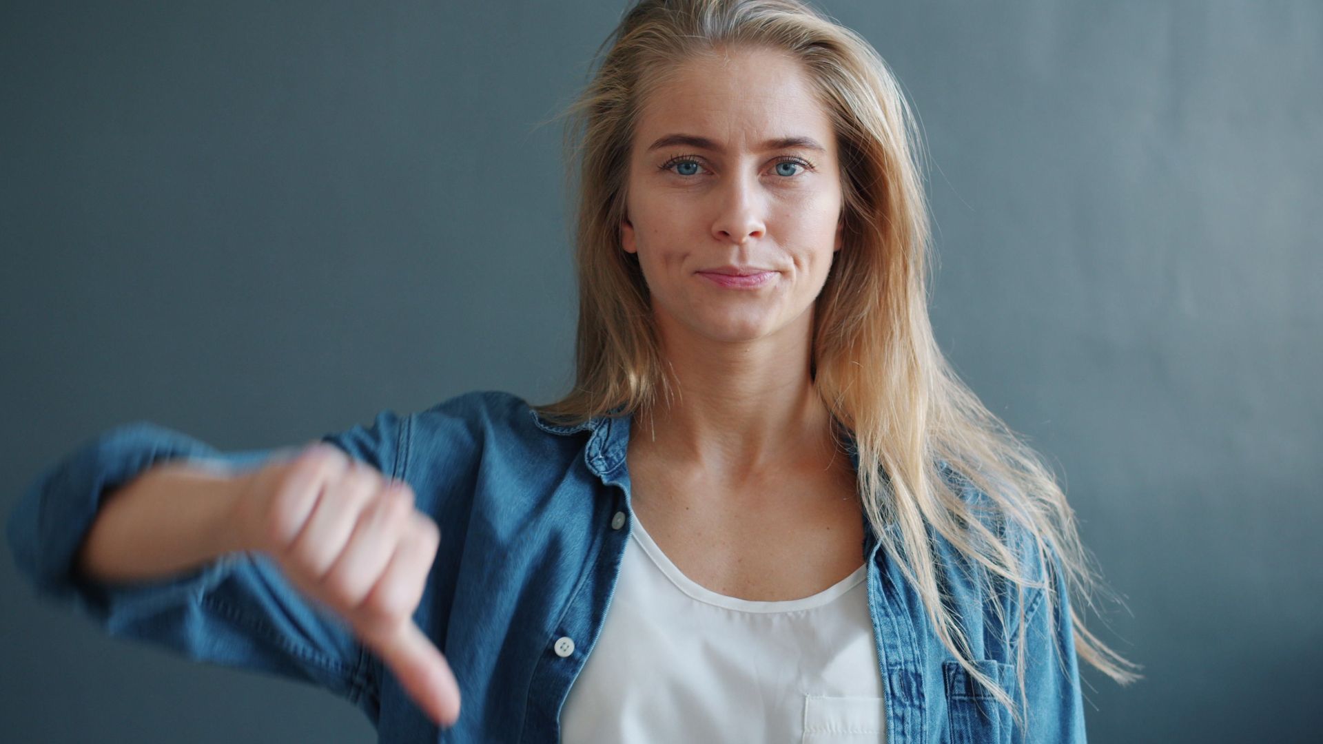 Confident young woman displaying a thumbs down sign against a neutral background.