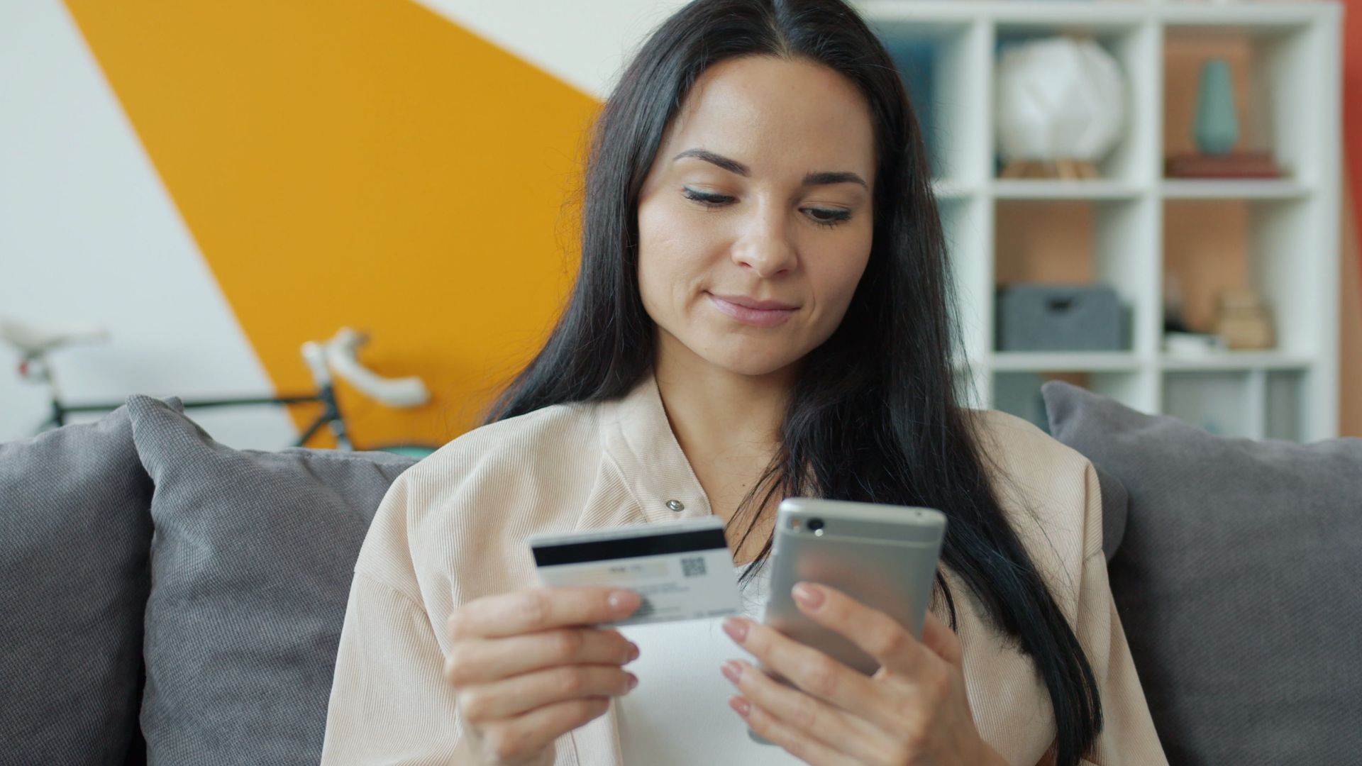 Woman sitting on sofa shopping online with mobile and credit card.