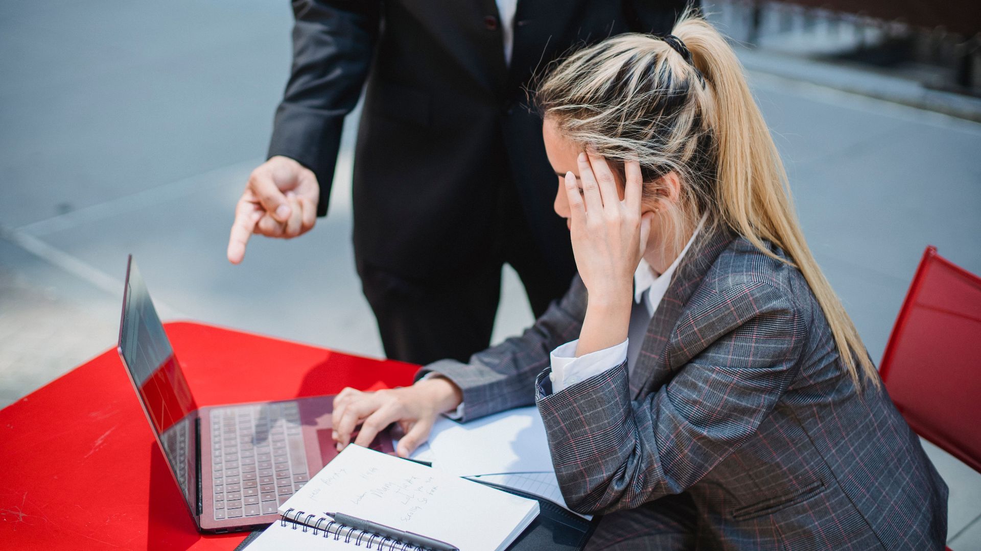 Business professionals discussing work on a laptop at an outdoor red table.