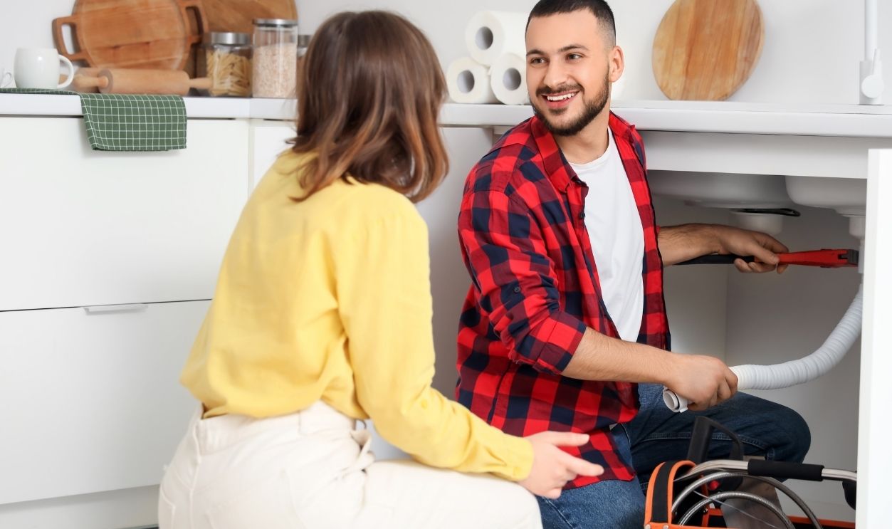 Young woman and plumber repairing sink pipe in kitchen
