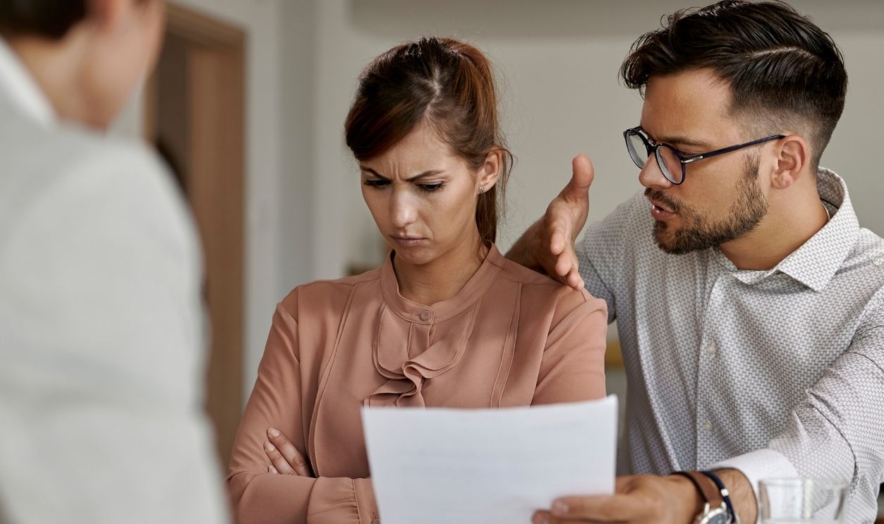 Young man trying to talk with his stubborn wife while analyzing lease agreement on a meeting with real estate agent.