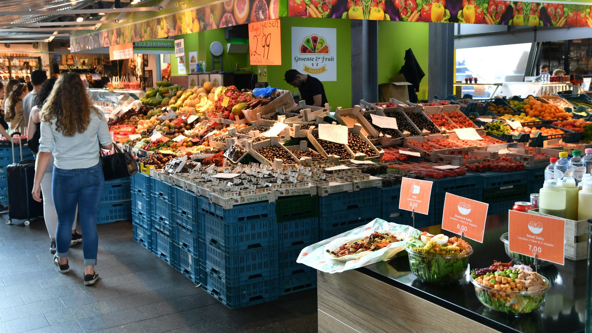 a woman walking through a market filled with lots of food