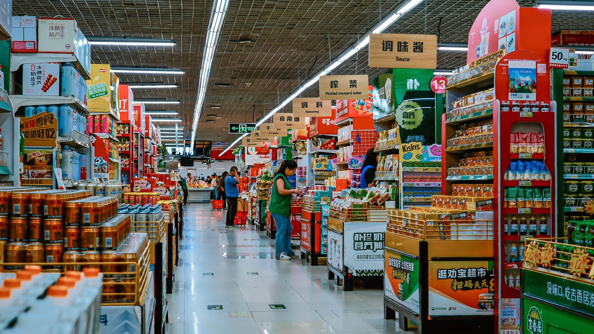 A vibrant supermarket aisle filled with diverse products and shoppers under bright lighting.