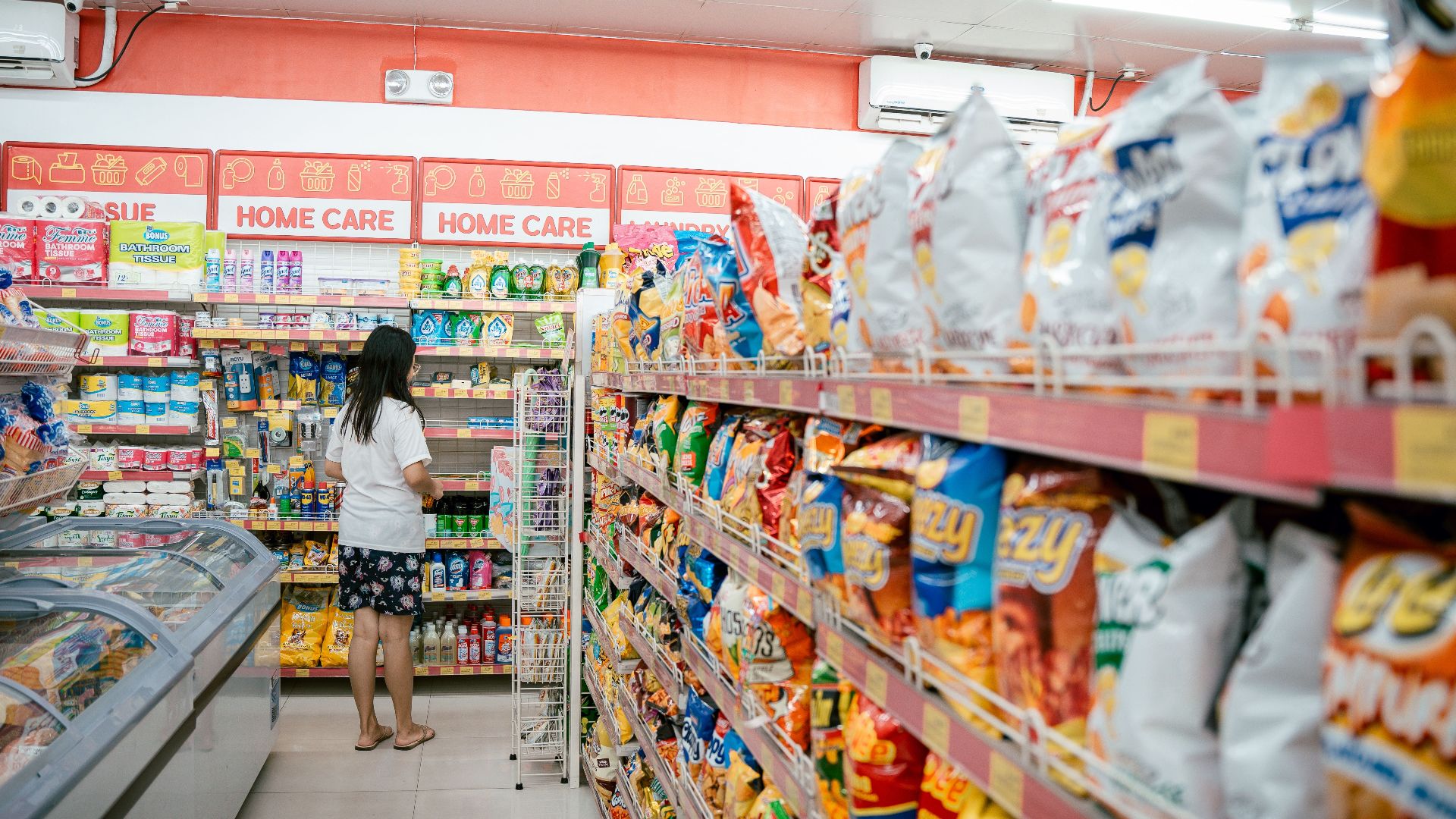 A woman browsing snack shelves at a supermarket, surrounded by various chips packages.