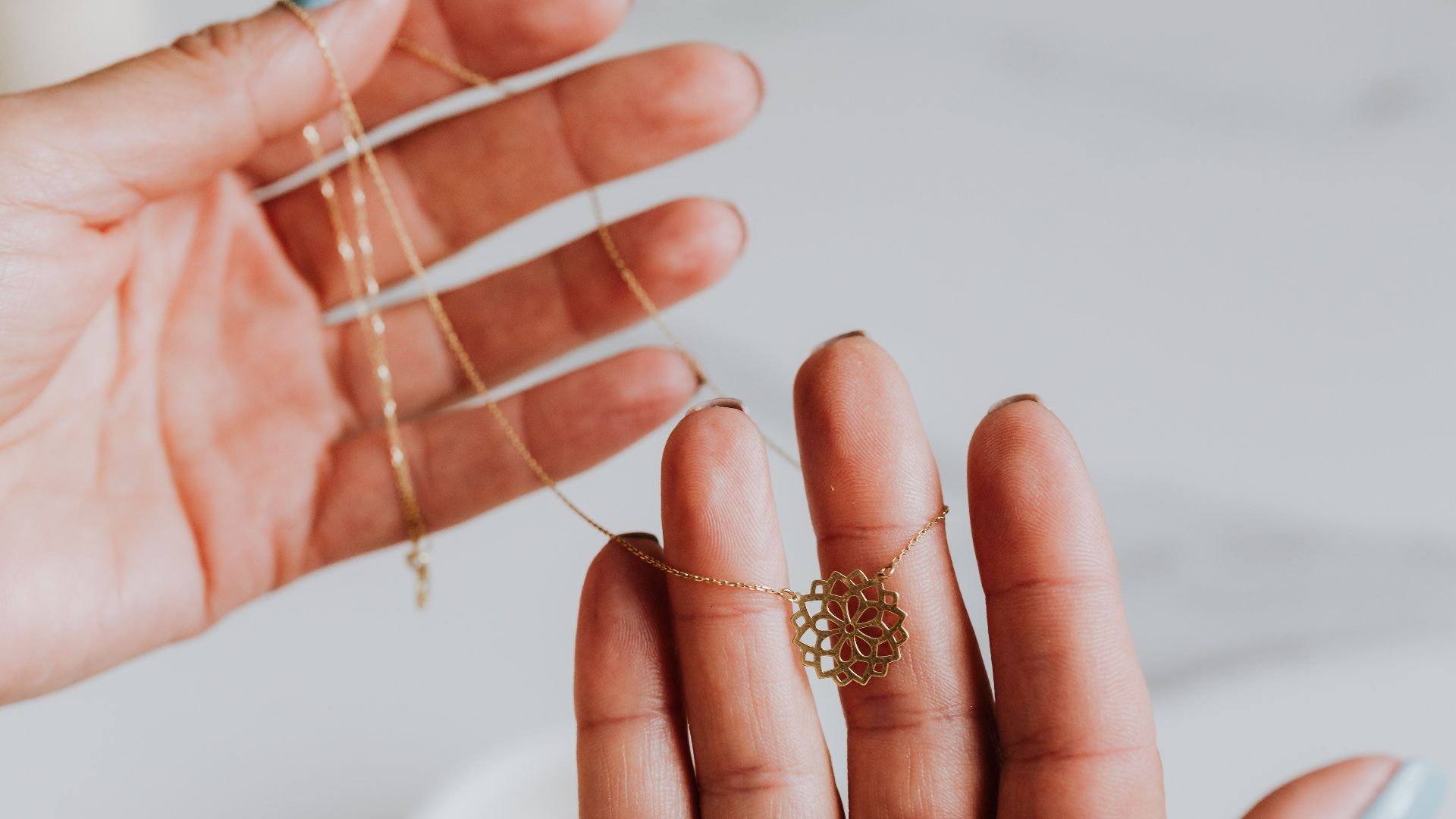 Close-up of a delicate gold necklace being held between hands, featuring an intricate pendant design.
