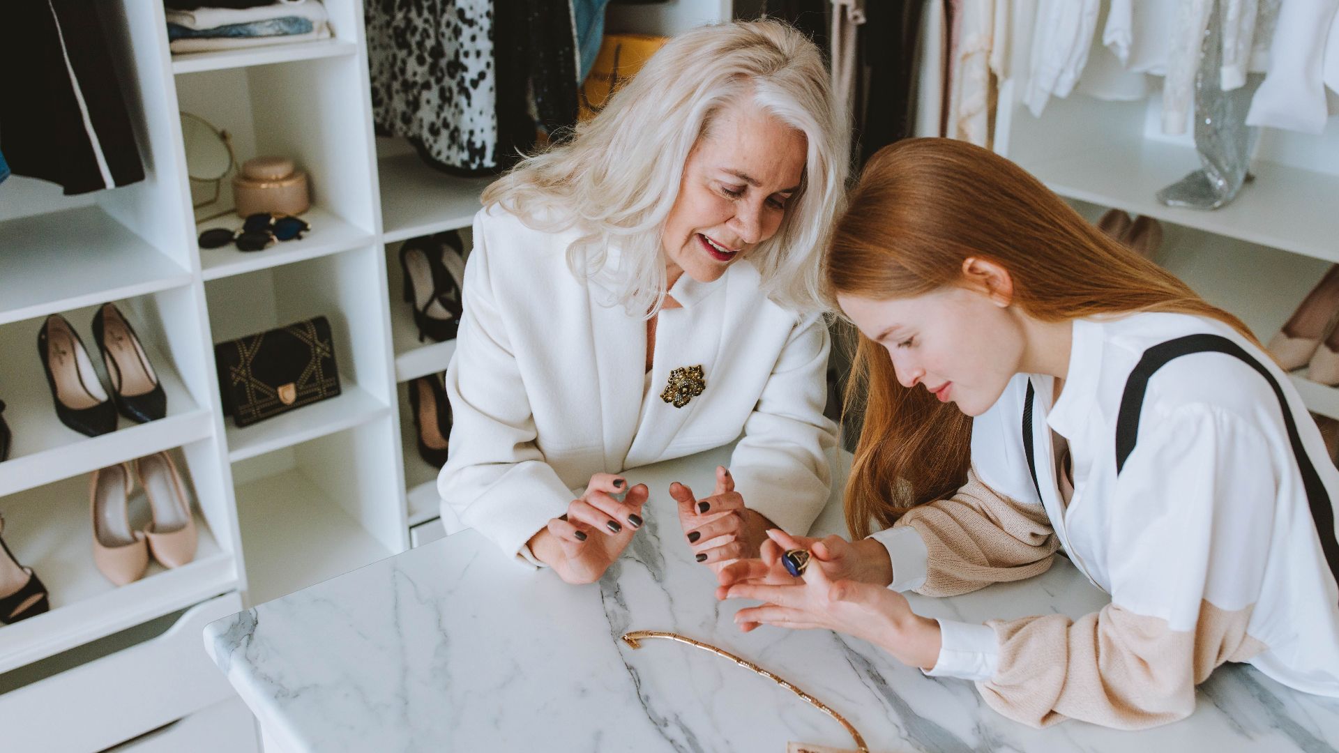 Two women exploring luxury jewelry in a stylish wardrobe setting.