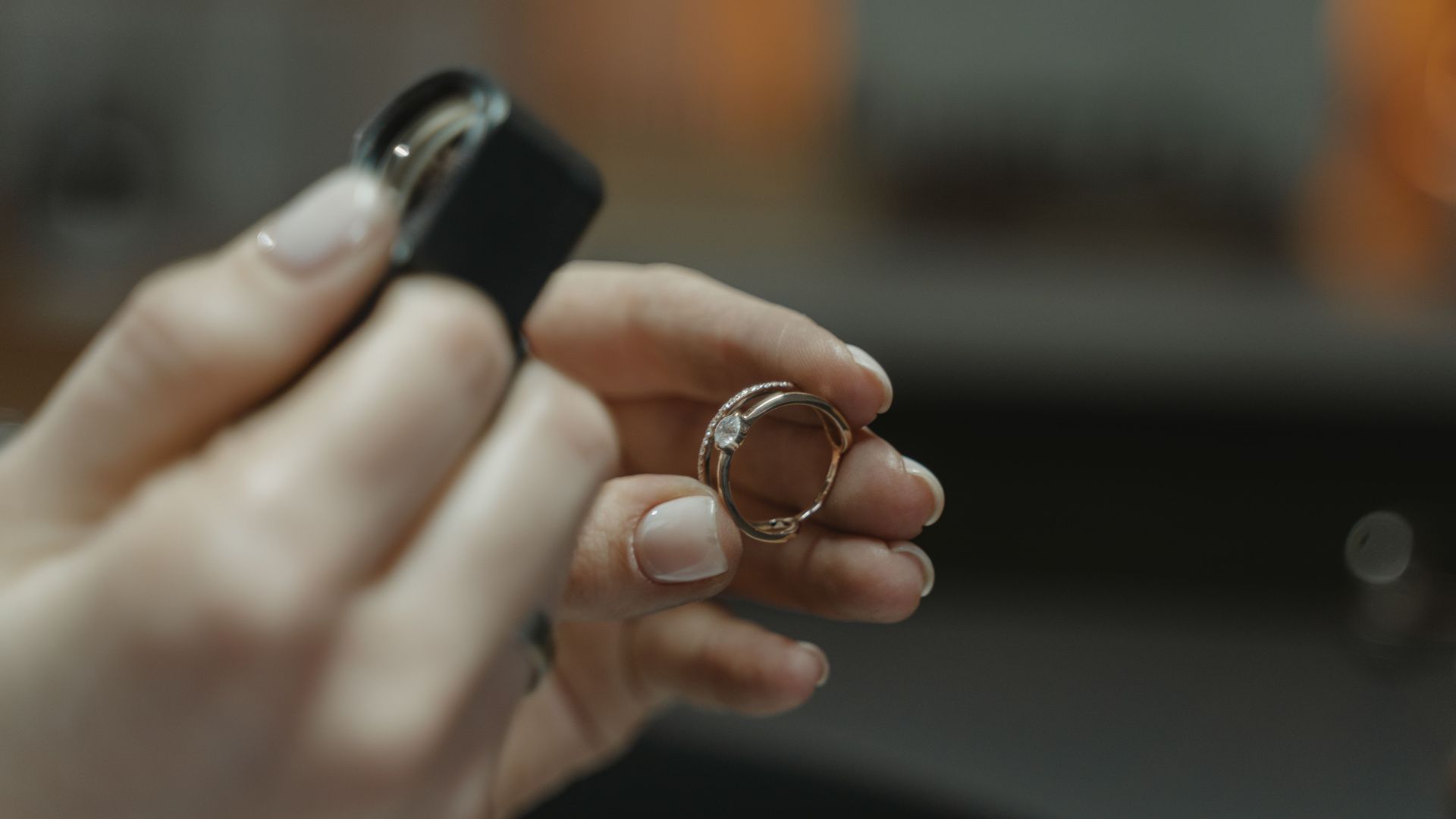 Close-up of a jeweler's hands holding a diamond ring and magnifying glass.
