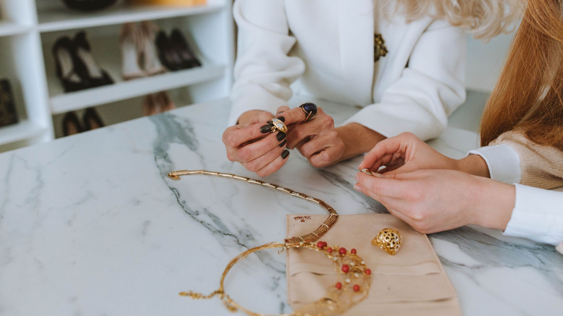 Two women examining luxury jewelry on a marble table in a boutique.