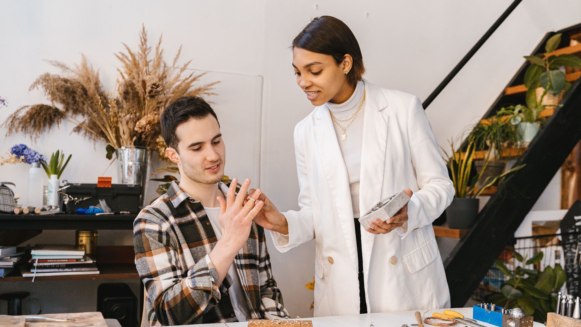 Two adults collaborating on a jewelry project in a modern indoor workspace.