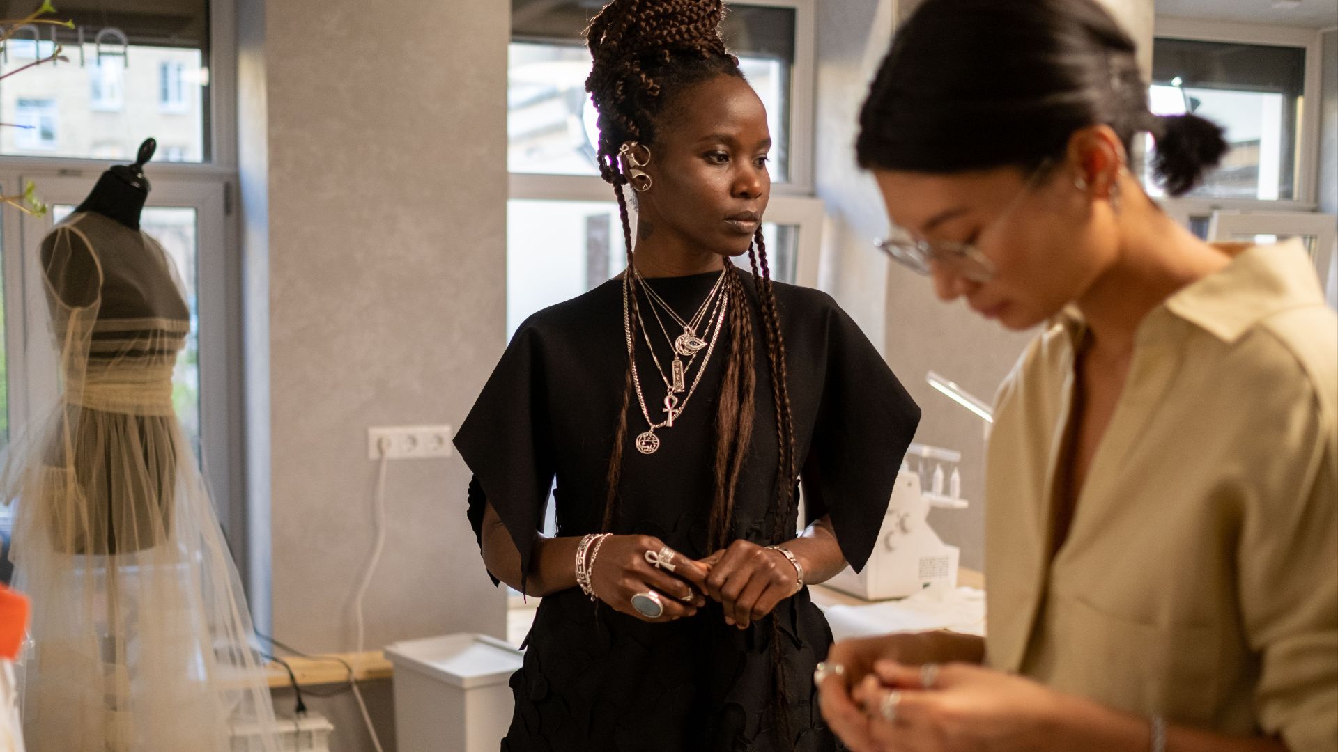 Two women fashion designers collaborating in a stylish studio environment with a mannequin and accessories.