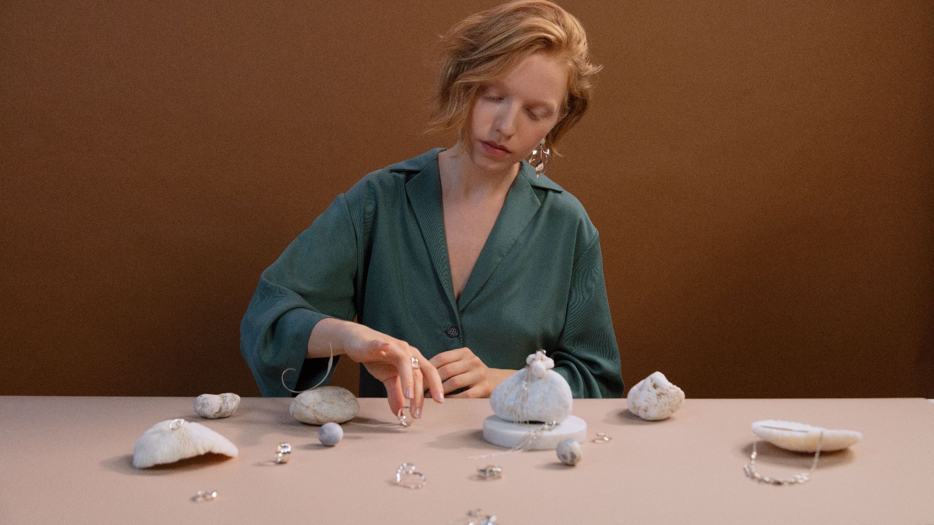 Caucasian woman arranging jewelry with rocks and stones in a minimalist setup indoors.