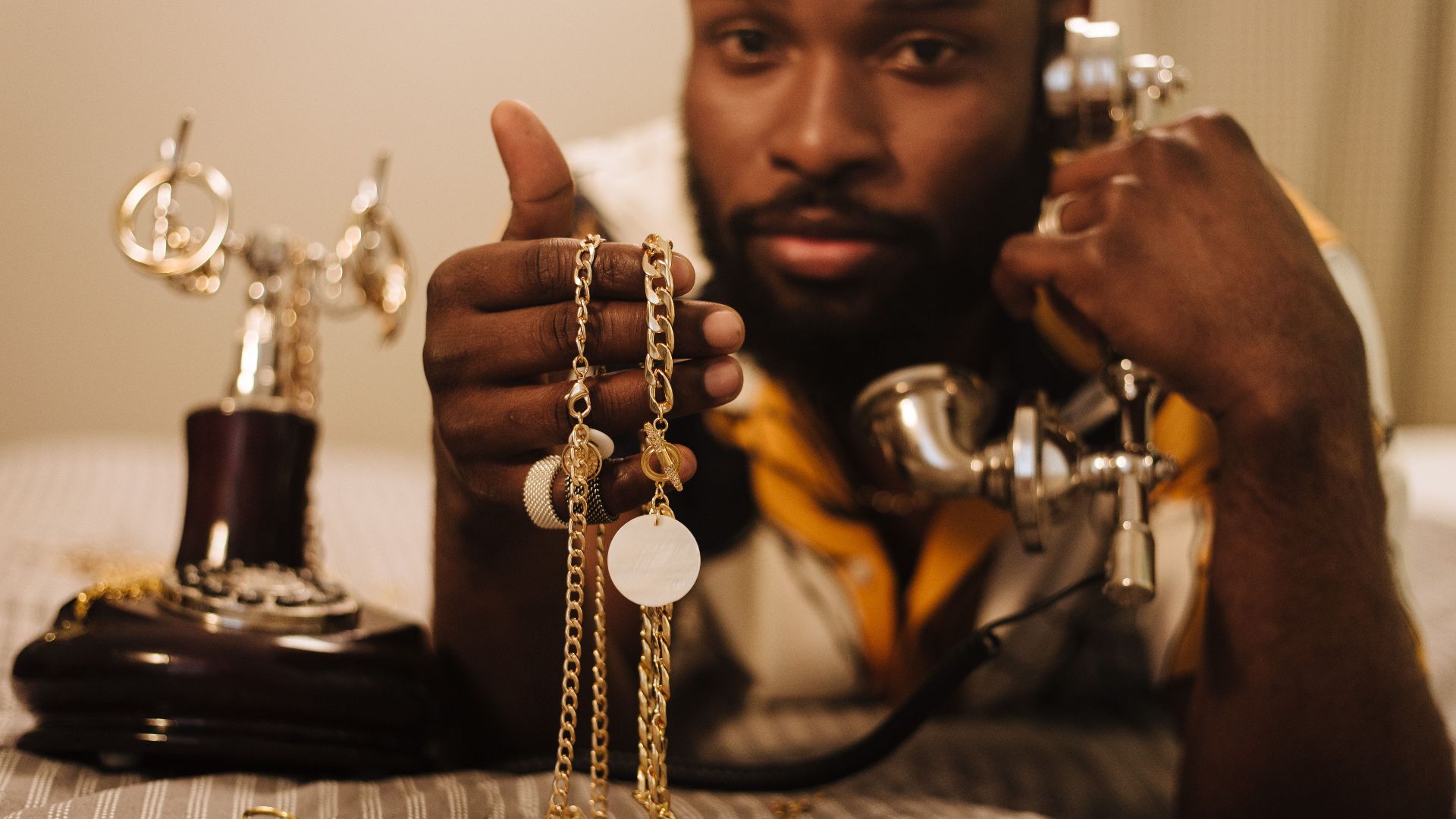 A man displays jewelry while using a vintage rotary phone. Stylish and elegant scene.