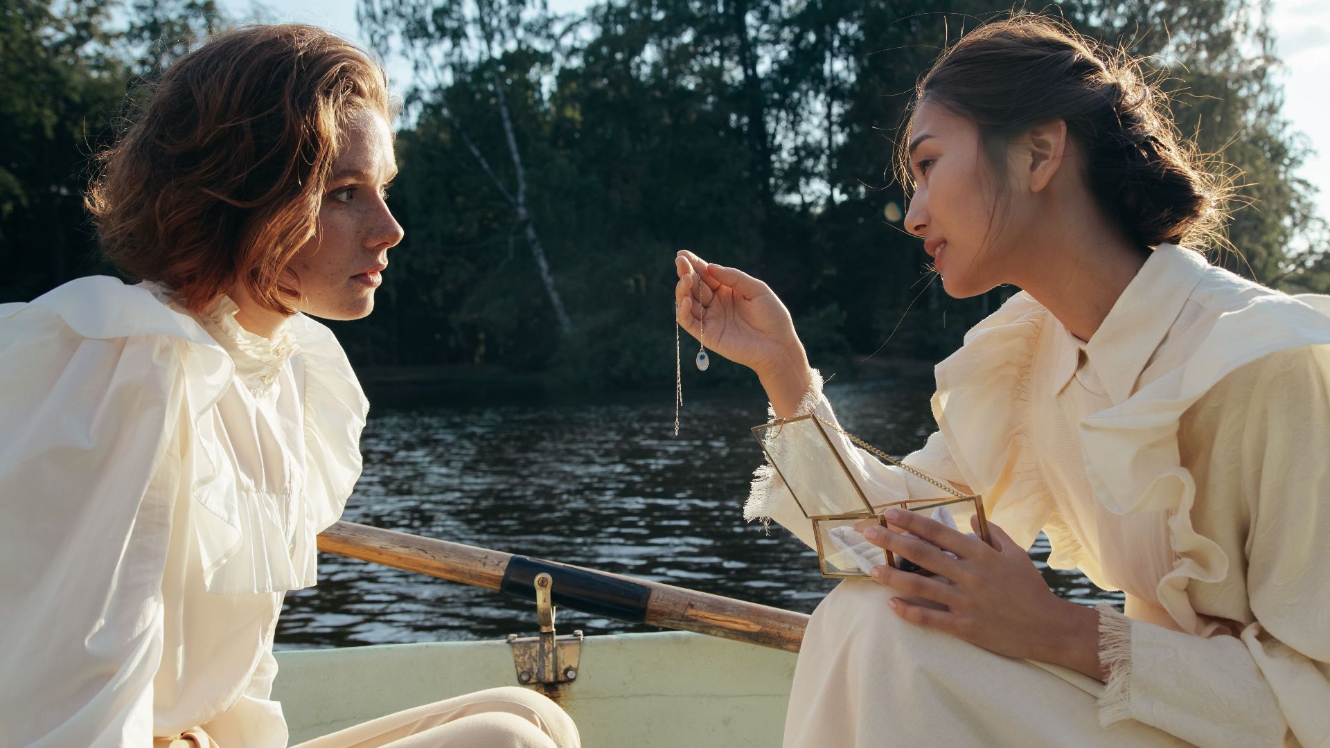 Two women in a boat share an intimate moment with a necklace under the sun.