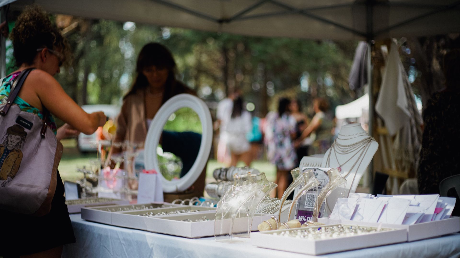 Outdoor jewelry market scene with diverse people browsing various stalls under a tent.