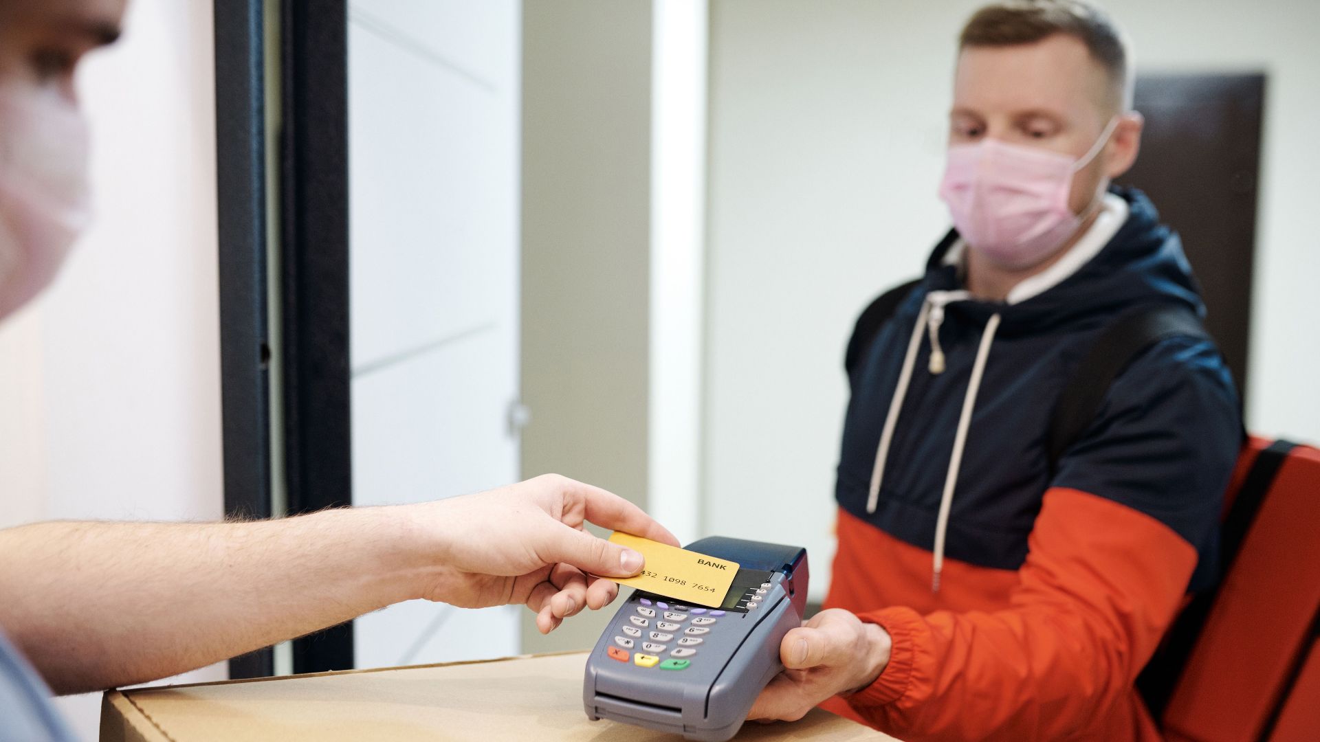 A man making a contactless payment for food delivery, both wearing face masks for safety.