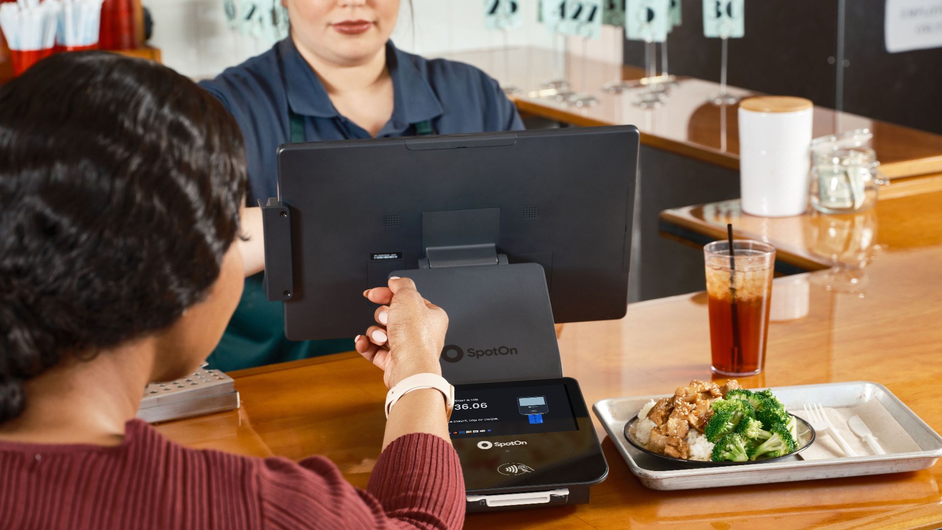 A customer uses smartwatch for contactless payment at a restaurant with SpotOn POS system.