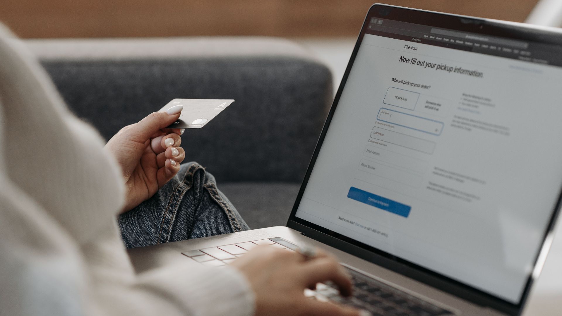 Woman holding credit card shopping online on a laptop from a couch.