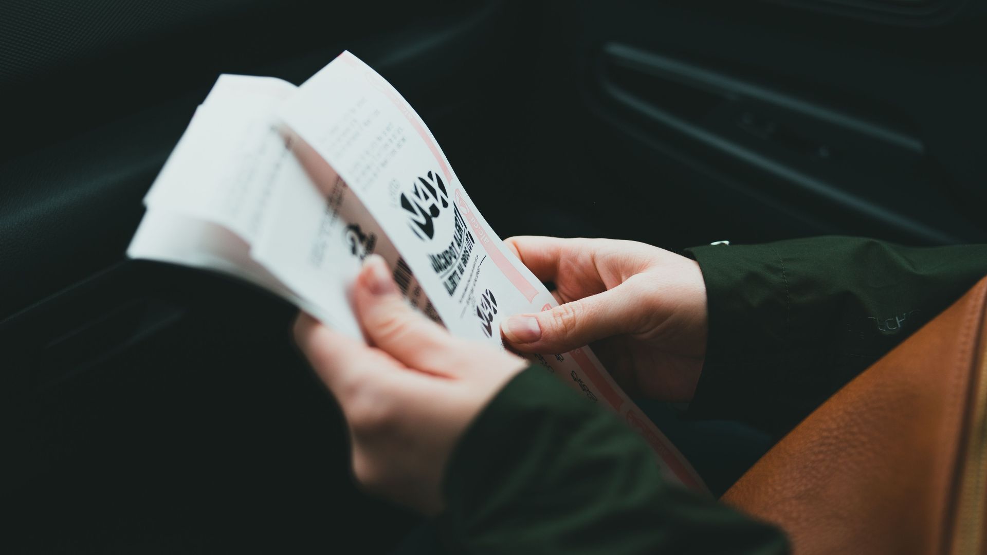 Close-up of hands holding a brochure inside a car, creating an intimate and focused scene.