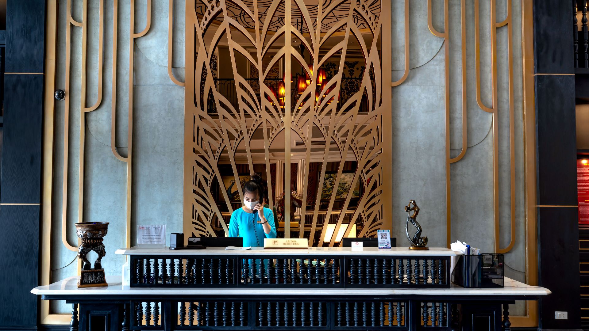 Luxurious hotel reception area with intricate design and a female receptionist at work.
