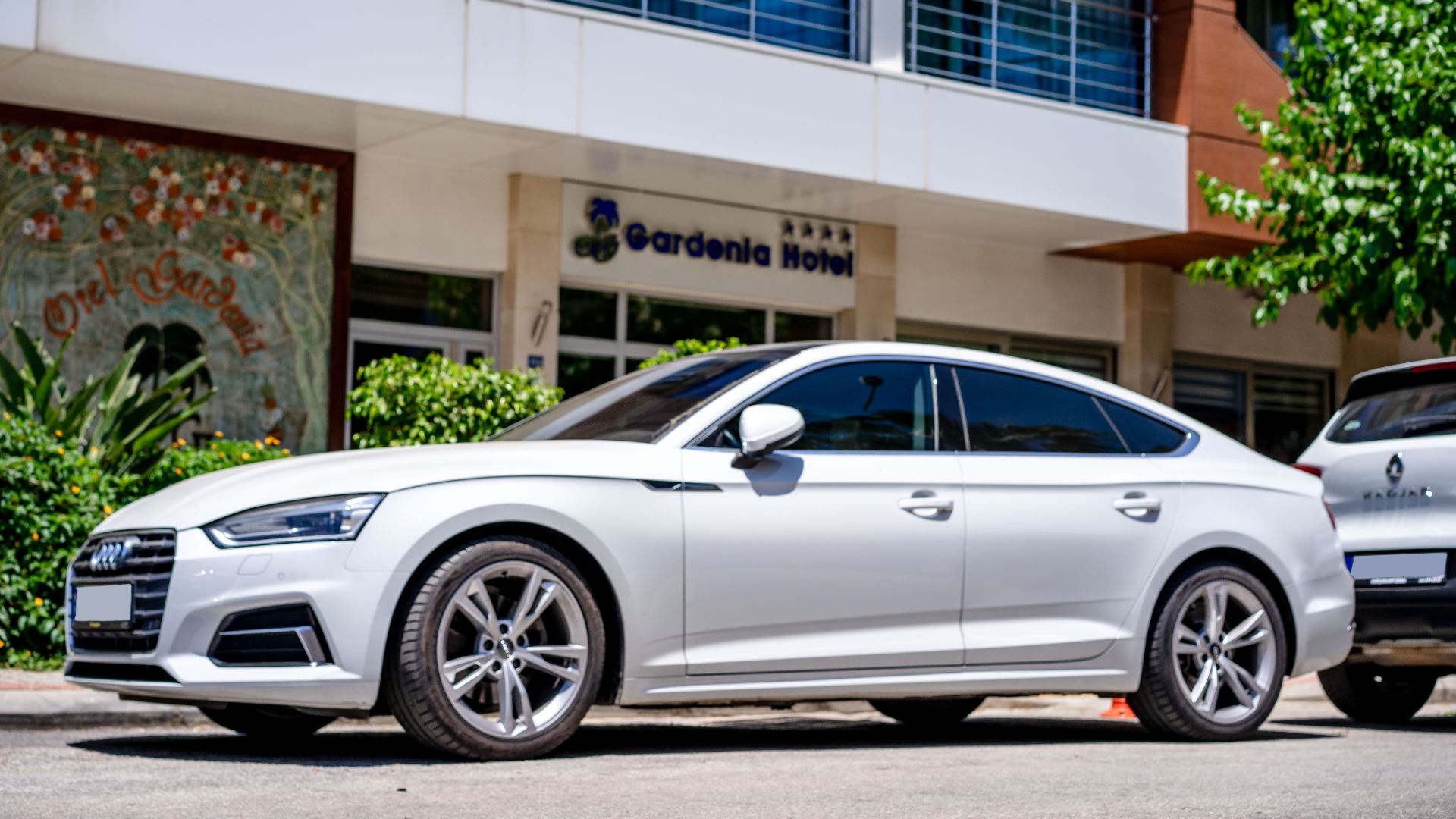 White luxury car parked in front of a hotel with modern architecture.