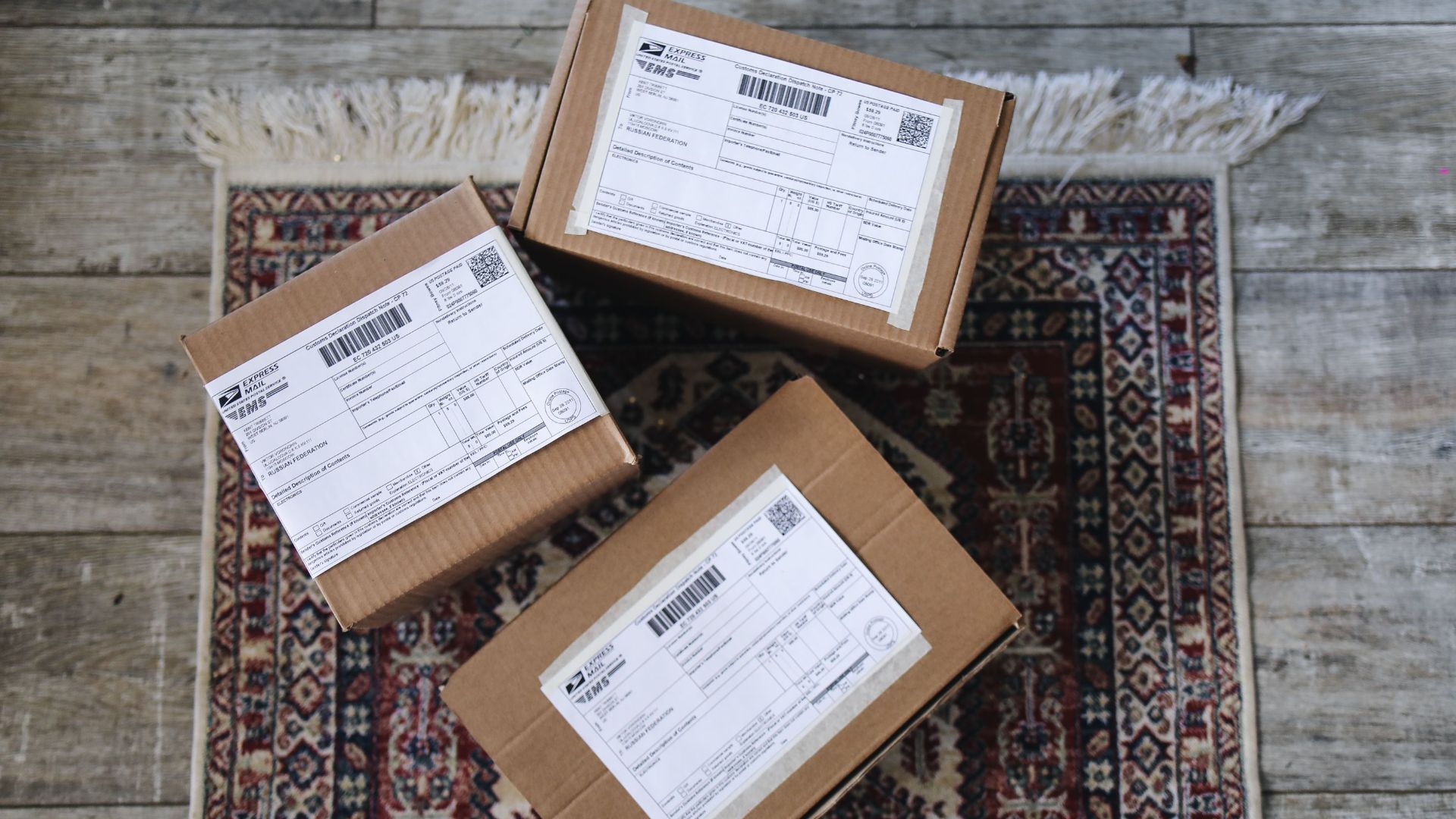 Three labeled delivery boxes placed on a decorative rug over a wooden floor.