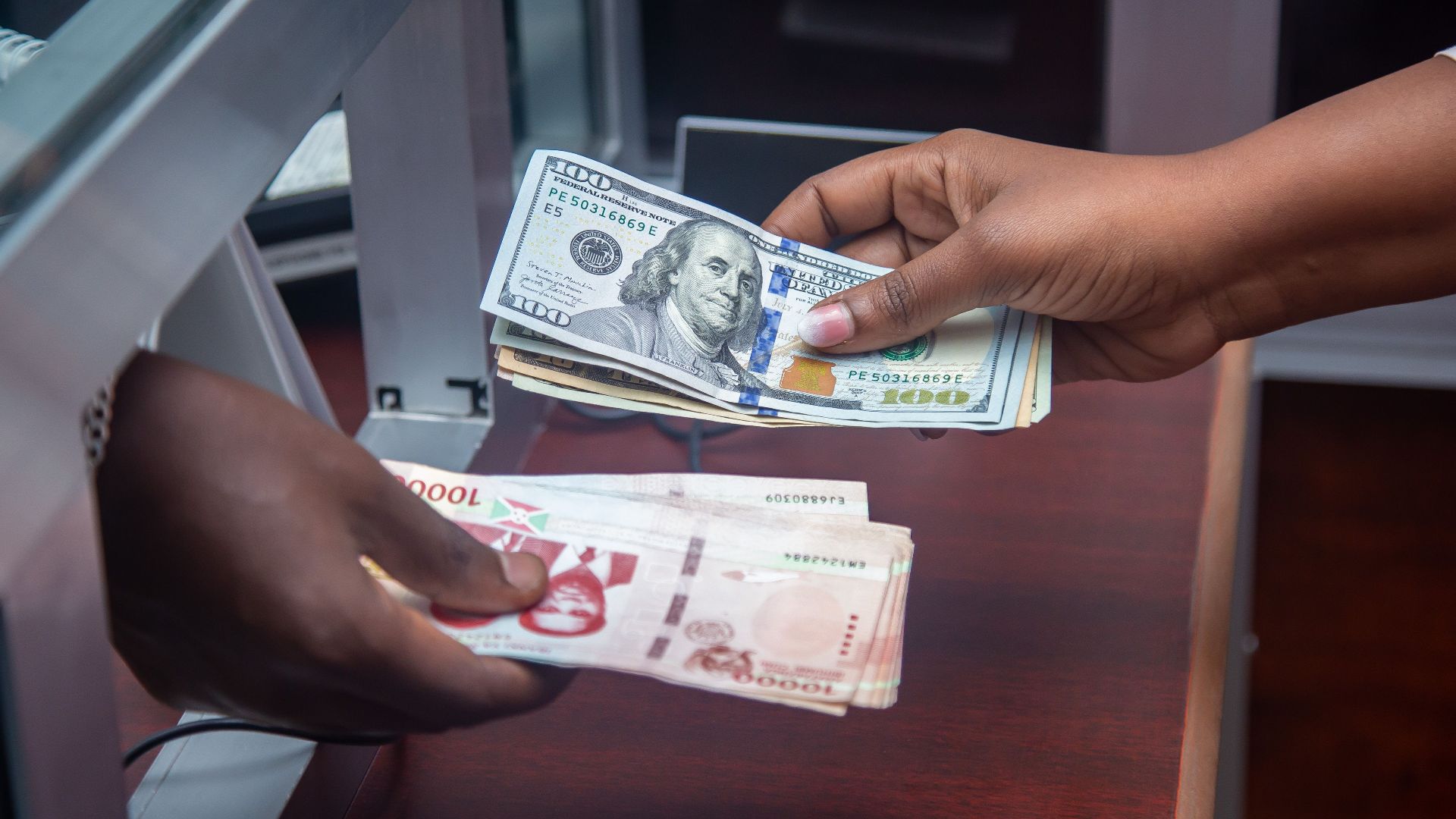 Hands exchanging US and local currency at a bank counter, signifying international finance.
