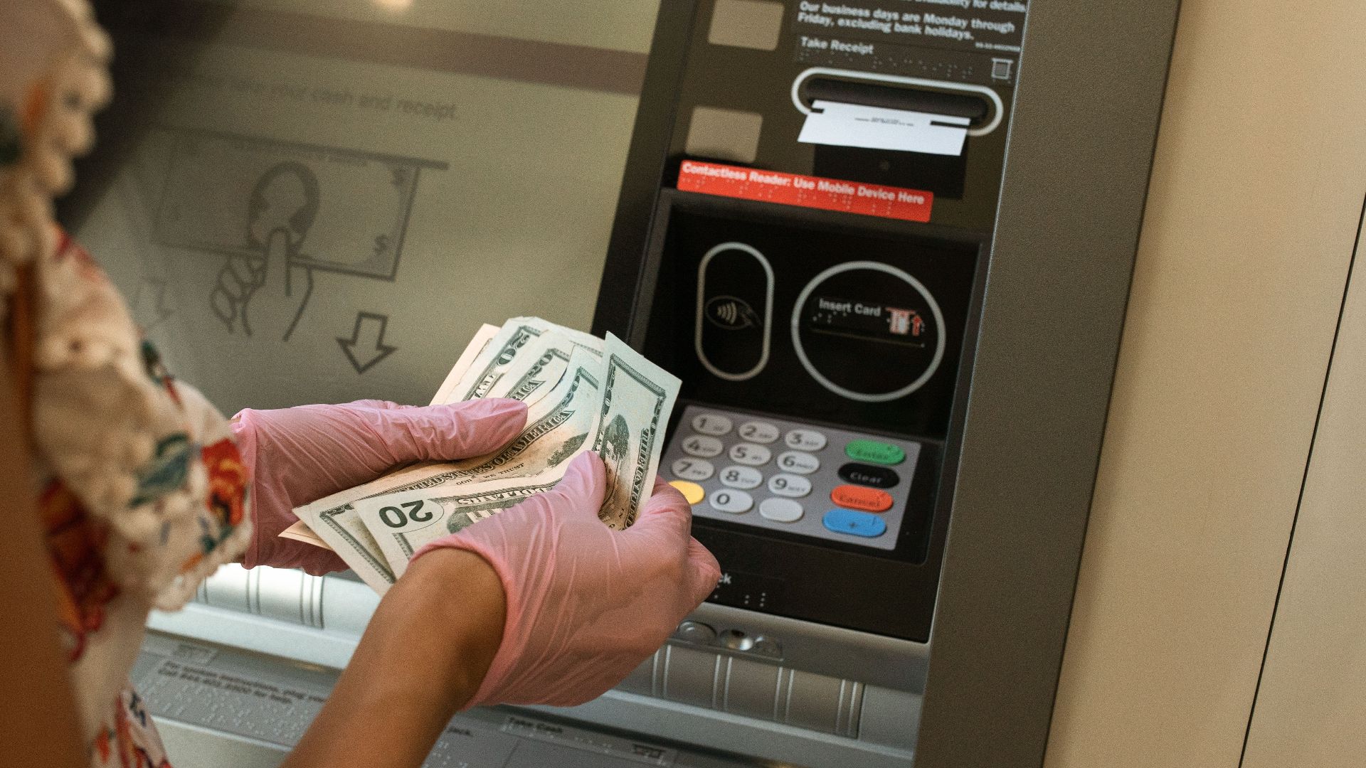 A person wearing gloves withdraws cash from an ATM, ensuring hygiene.