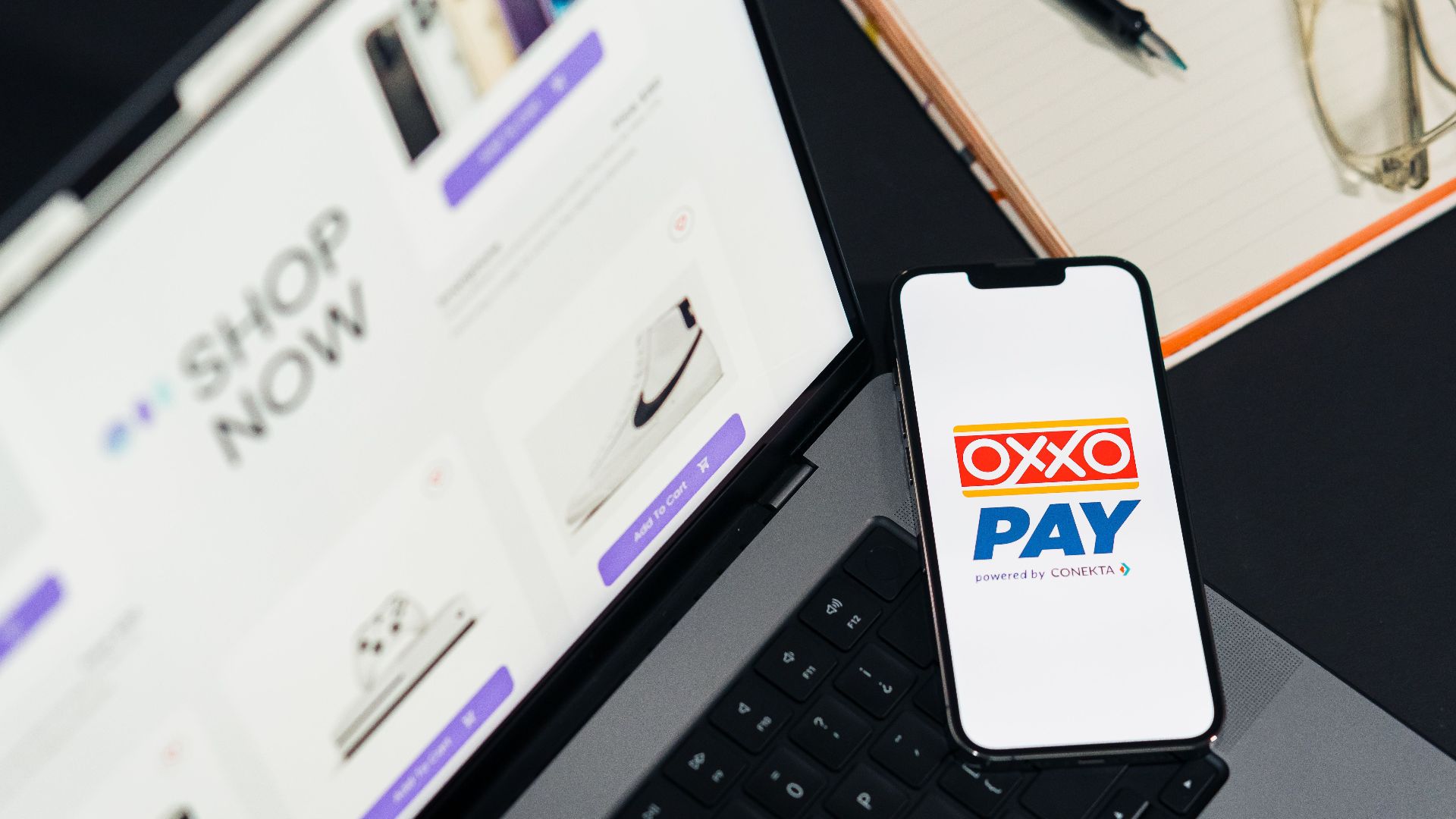 A mobile phone with OXXO Pay on a laptop used for online shopping.