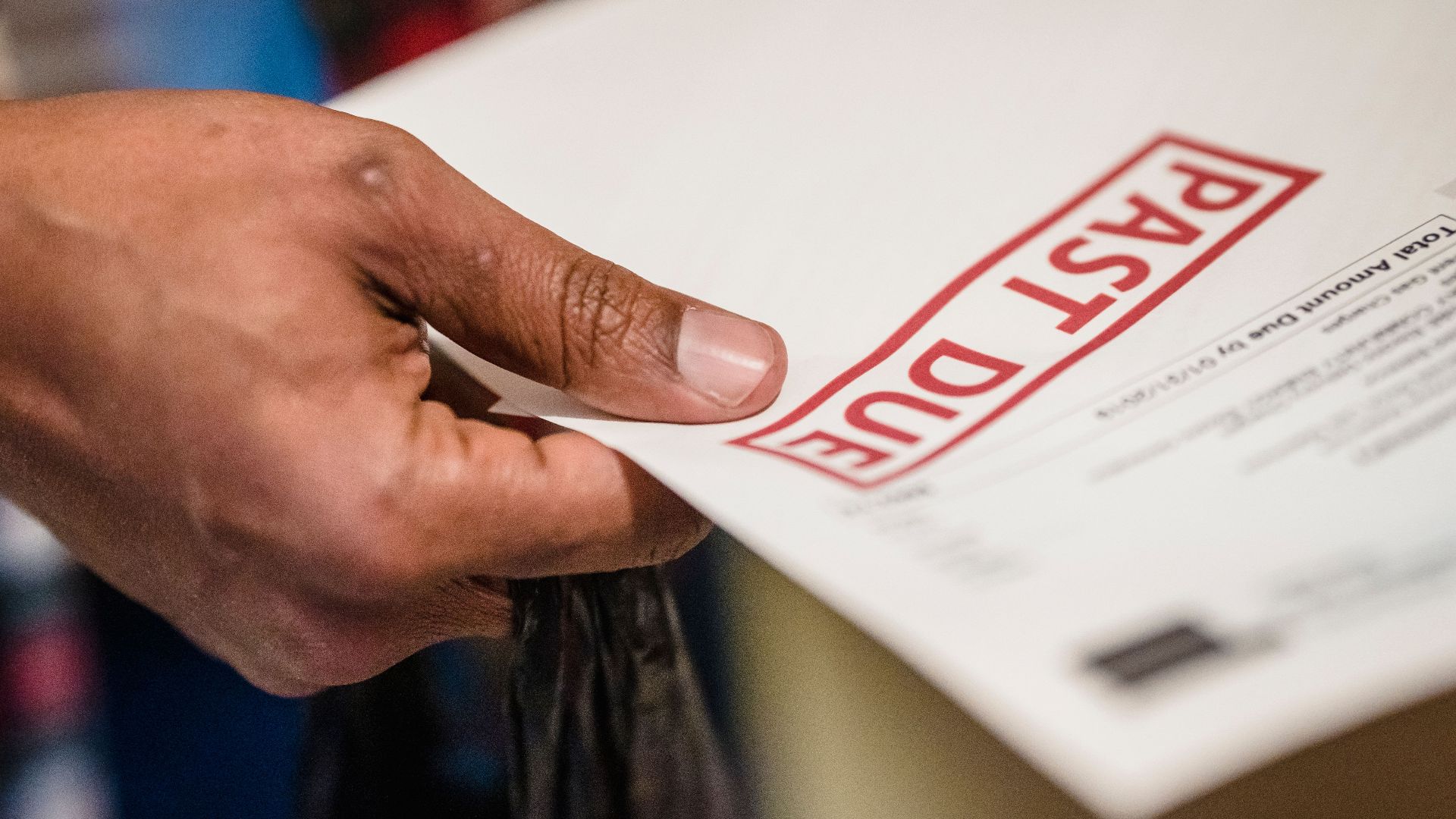 A close-up of a hand holding a document with a 'Past Due' stamp, highlighting financial urgency.